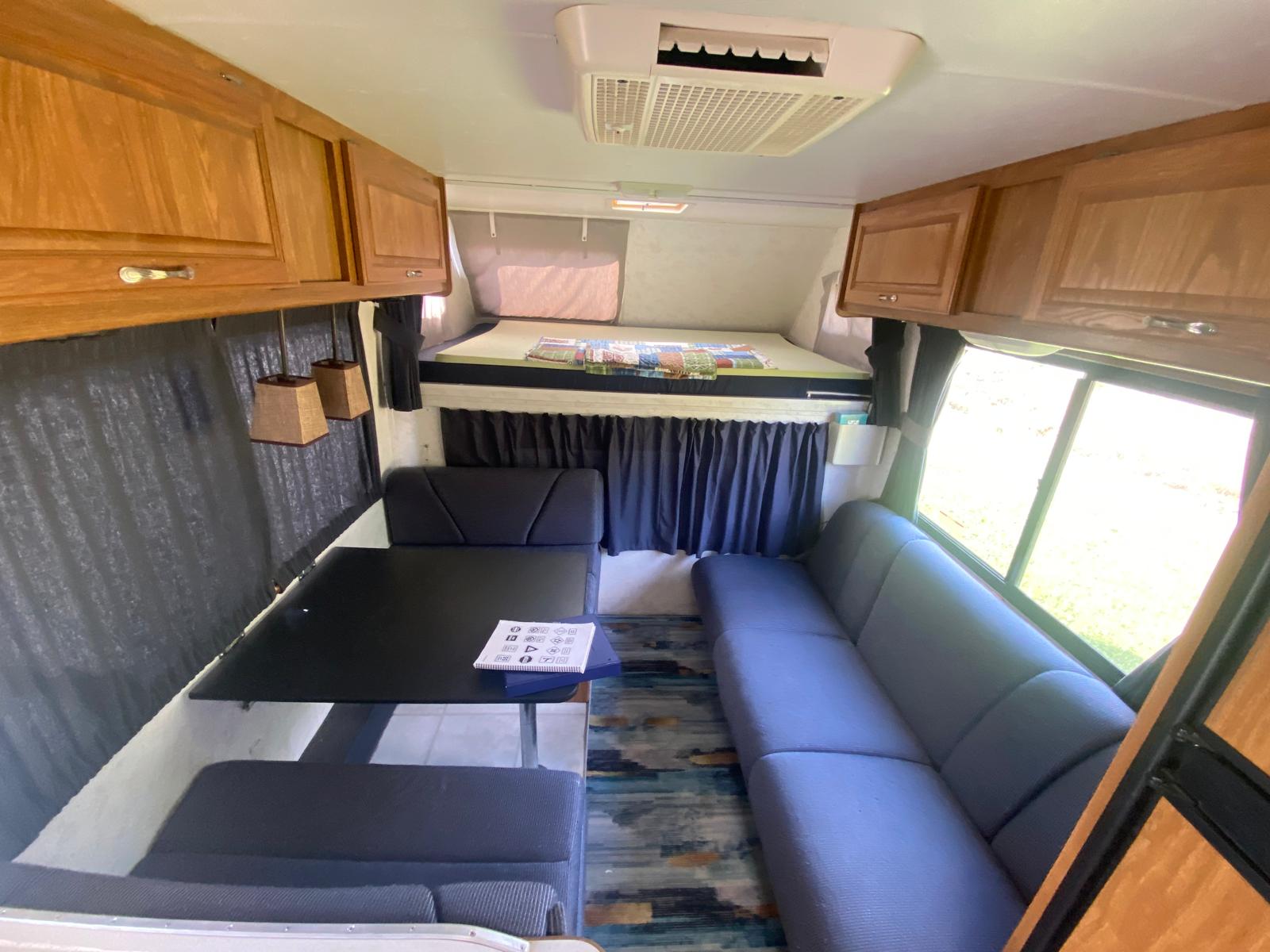 Spacious RV rental interior with dinette, sofa, and overhead bunk. Perfect for road trips and camping.. Thor Majestic 19G 2004