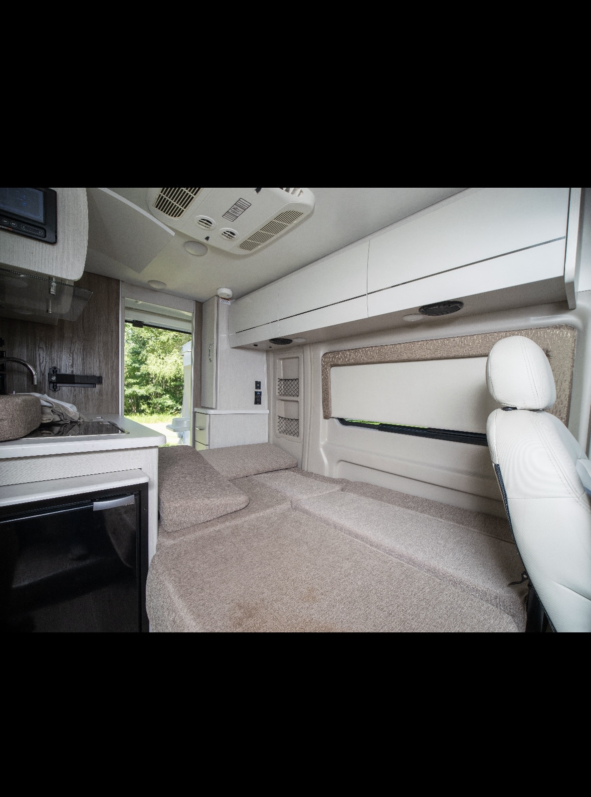 Inside an RV rental: versatile camper interior with kitchen, modular bed, storage, and driver's seat.. Thor Rize 2022