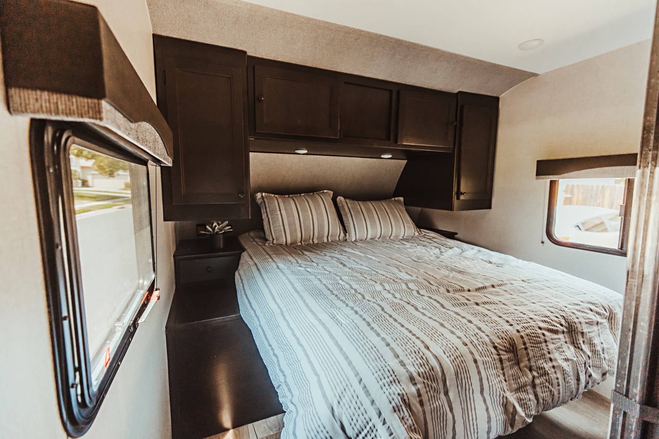 Cozy RV rental bedroom with a striped bed, overhead cabinets, and windows, ready for your next adventure.. Highland Mesa Ridge 2021