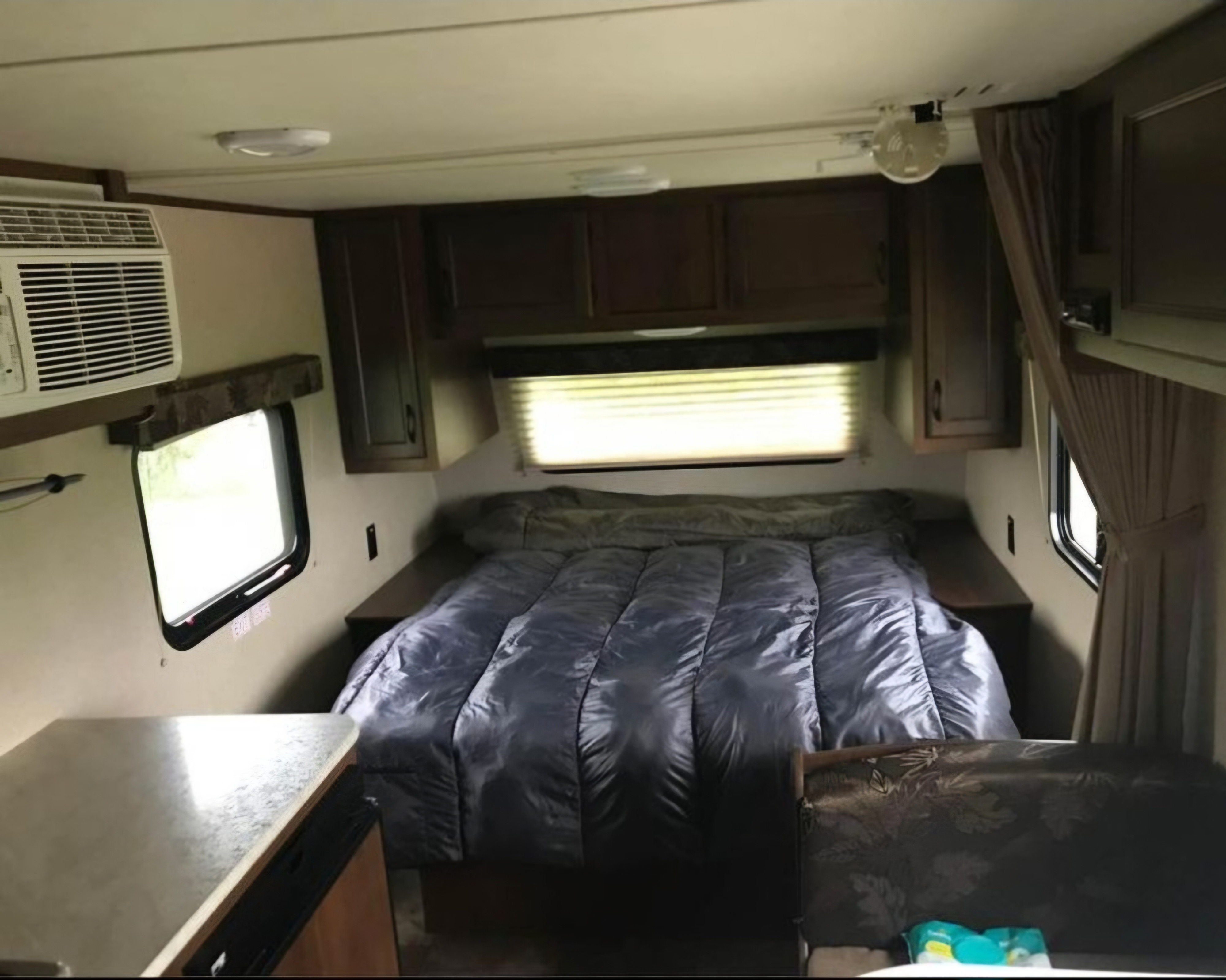 Cozy RV rental bedroom with a comfy bed, overhead cabinets, and window with an AC unit for your next adventure.. Jayco Jay Flight SLX 2015