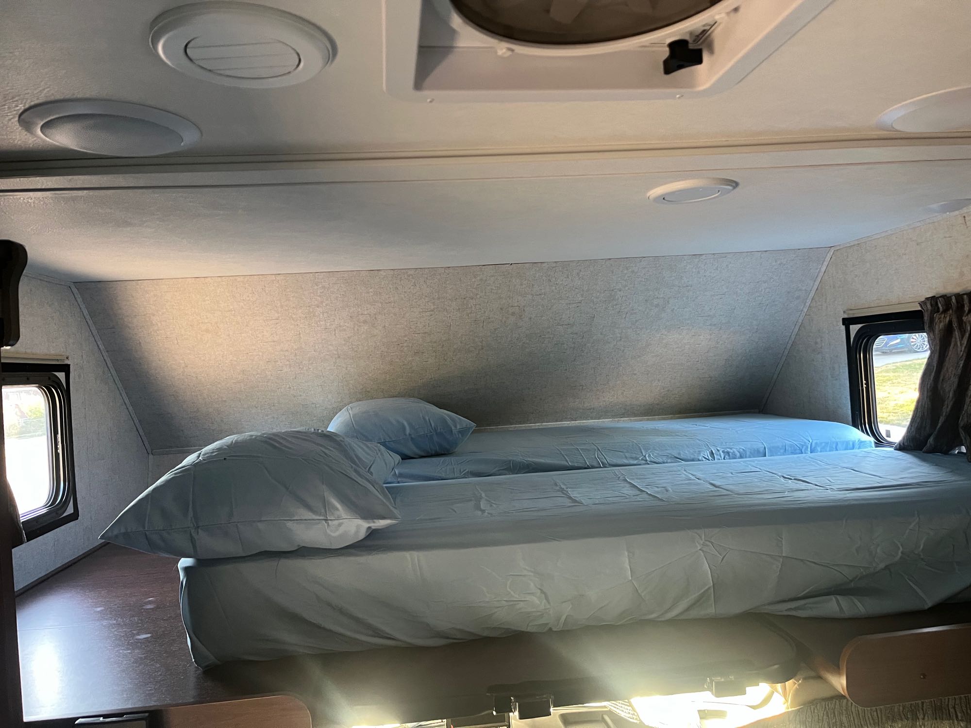 Cozy RV rental sleeping area with two side-by-side beds, light blue sheets, and ceiling vents for comfort.. Forest River Sunseeker 2018