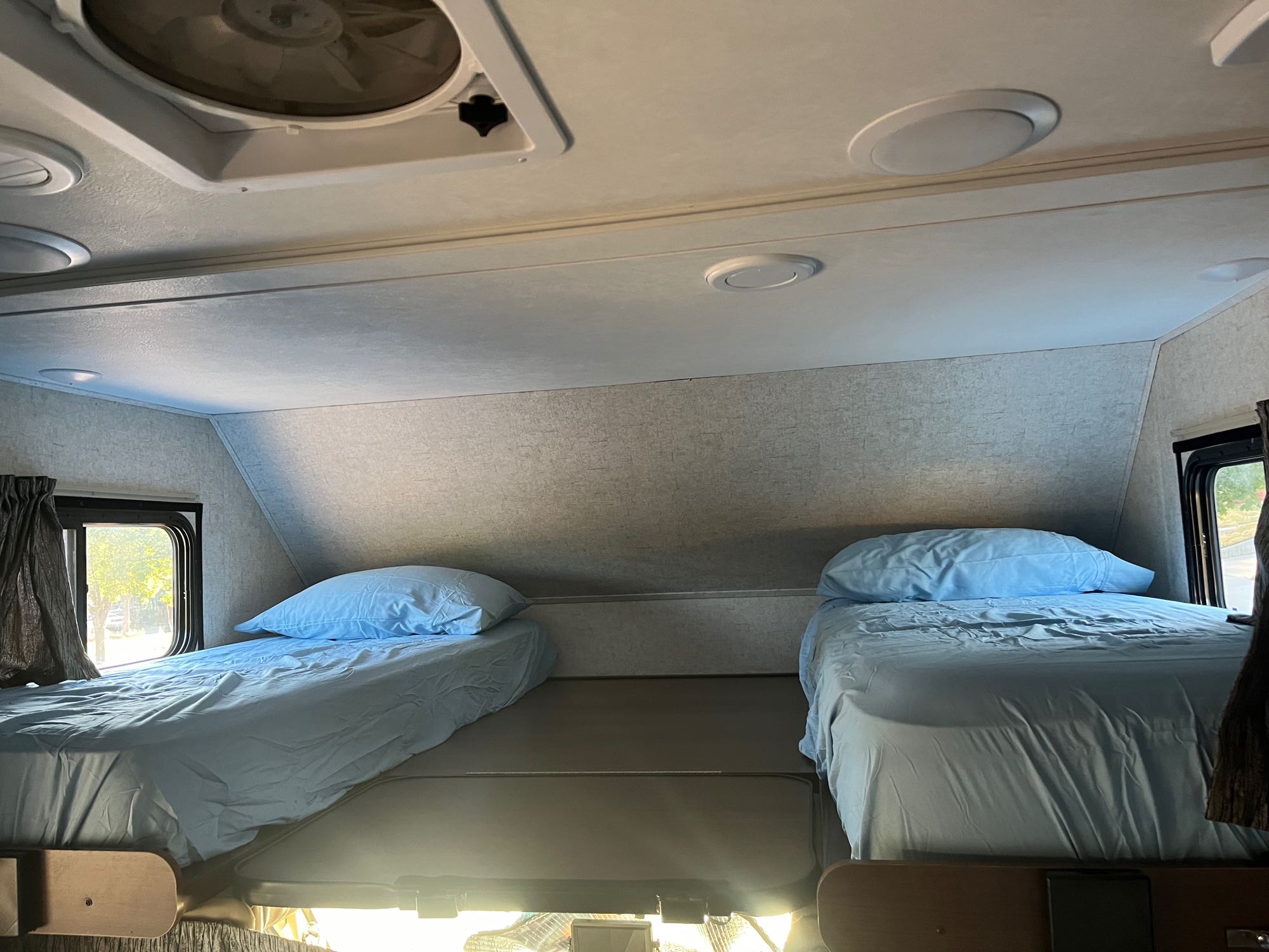 Inside an rv rental: The cab-over bunk has two beds with blue sheets, a ceiling fan, and overhead lighting.. Forest River Sunseeker 2018