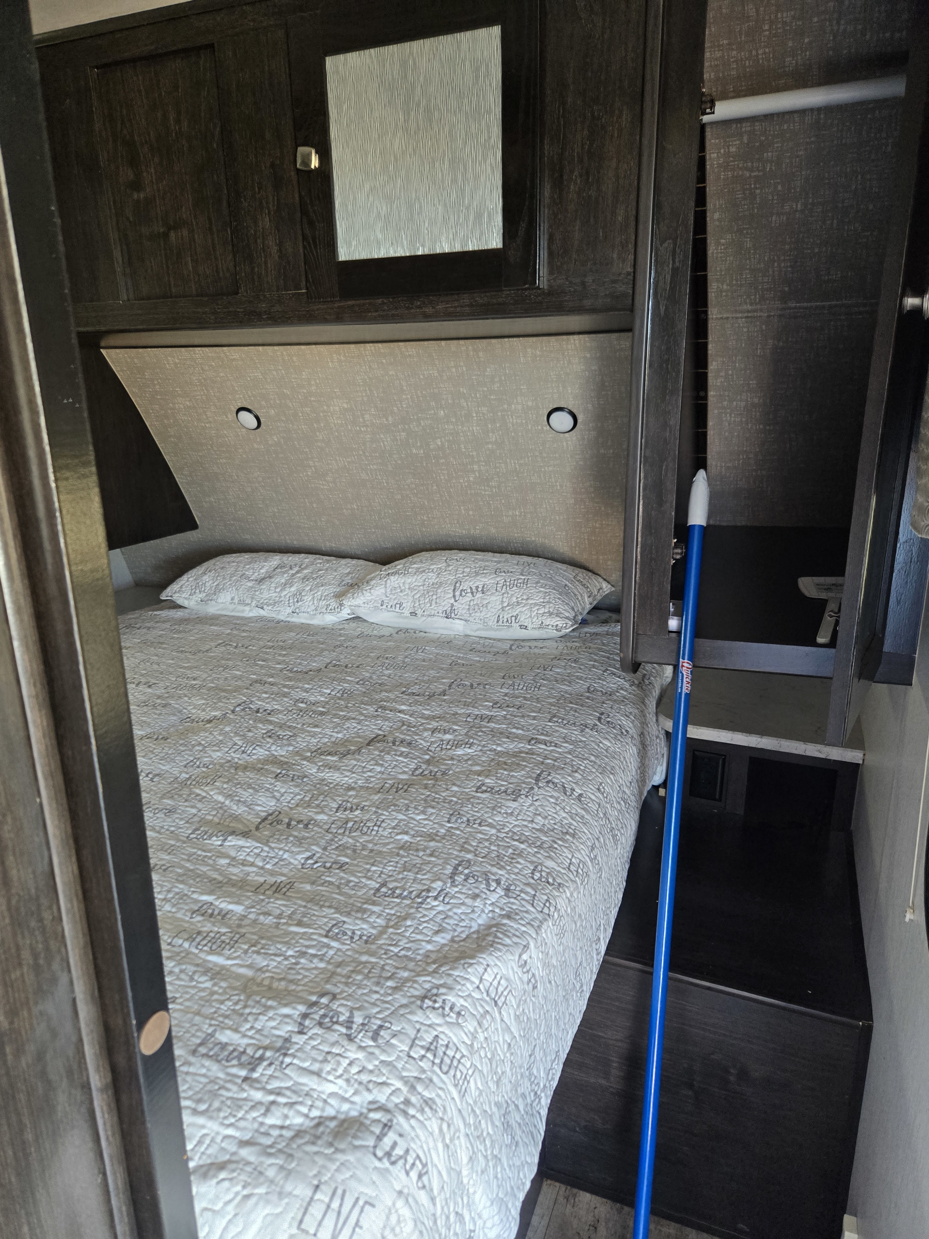 RV rental bedroom: cozy bed with quilted comforter, lighted headboard, and built-in dark wood cabinets.. Heartland RVs North Trail 2018
