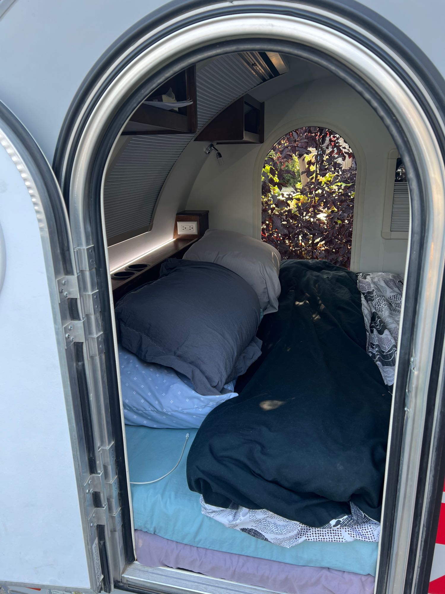 Inside this cozy RV rental, discover a comfortable bed, built-in shelf with outlets, and a unique arched window view.. nuCamp T@G 2018
