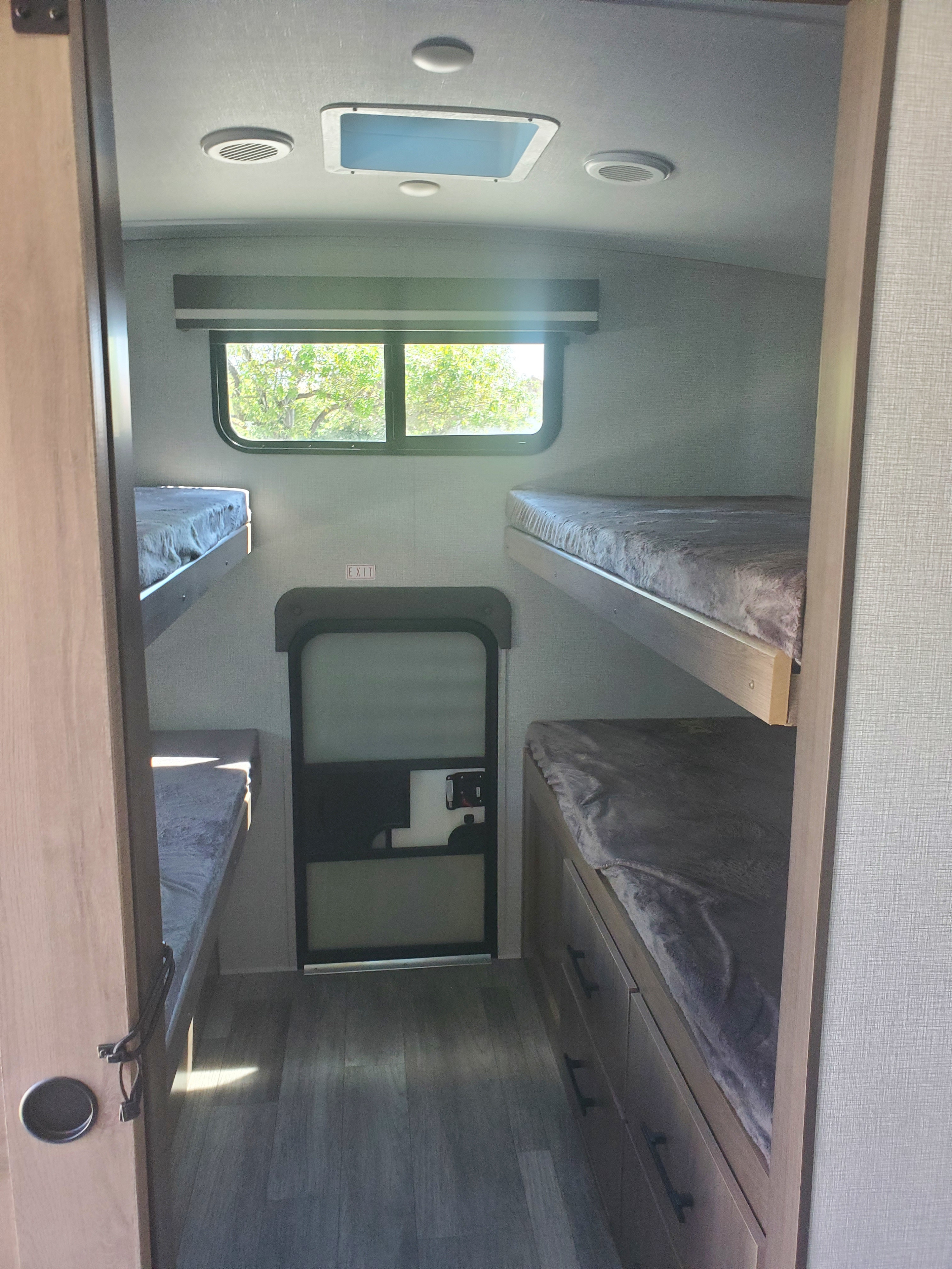 RV rental interior: Bunk beds on both sides, a window showcasing trees, an exit door, and storage below.. Grand Design Imagine 2023