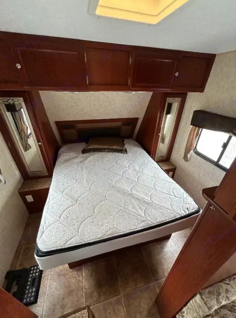 Cozy RV rental bedroom with a comfortable bed, overhead cabinets, and side mirrors. Perfect for travel!. Dutchmen Kodiak 2010