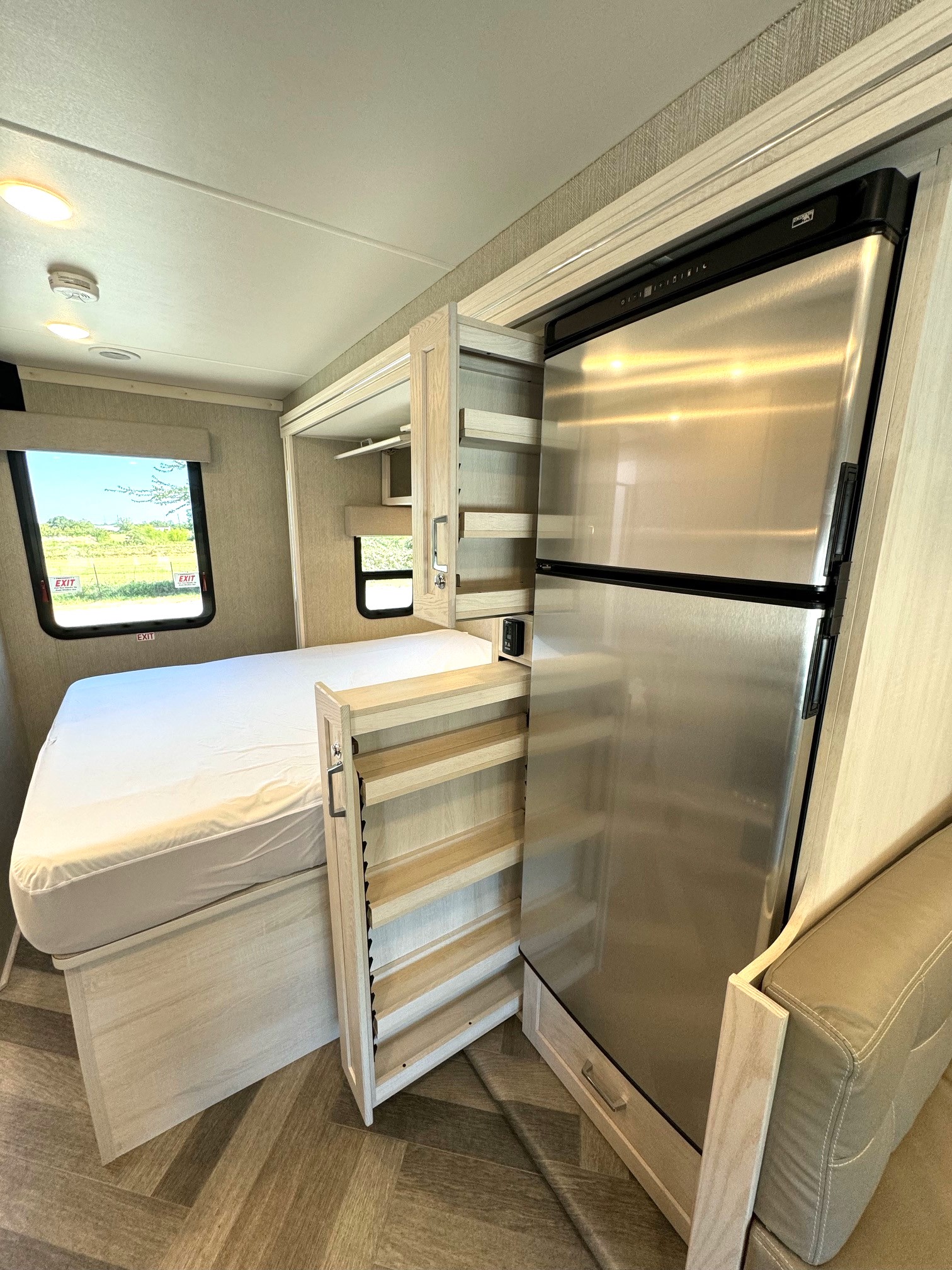 Compact RV rental interior featuring a bed, stainless steel refrigerator, and a pull-out pantry for efficient space.. Winnebago vita 2023