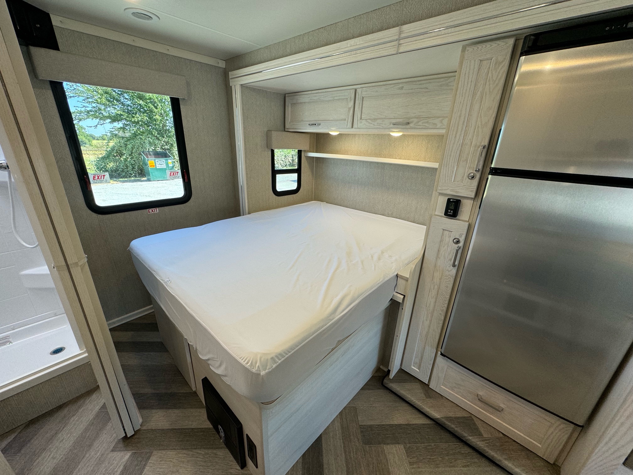 RV rental interior view: Compact bedroom with white bed, small fridge, shower, & window.. Winnebago vita 2023