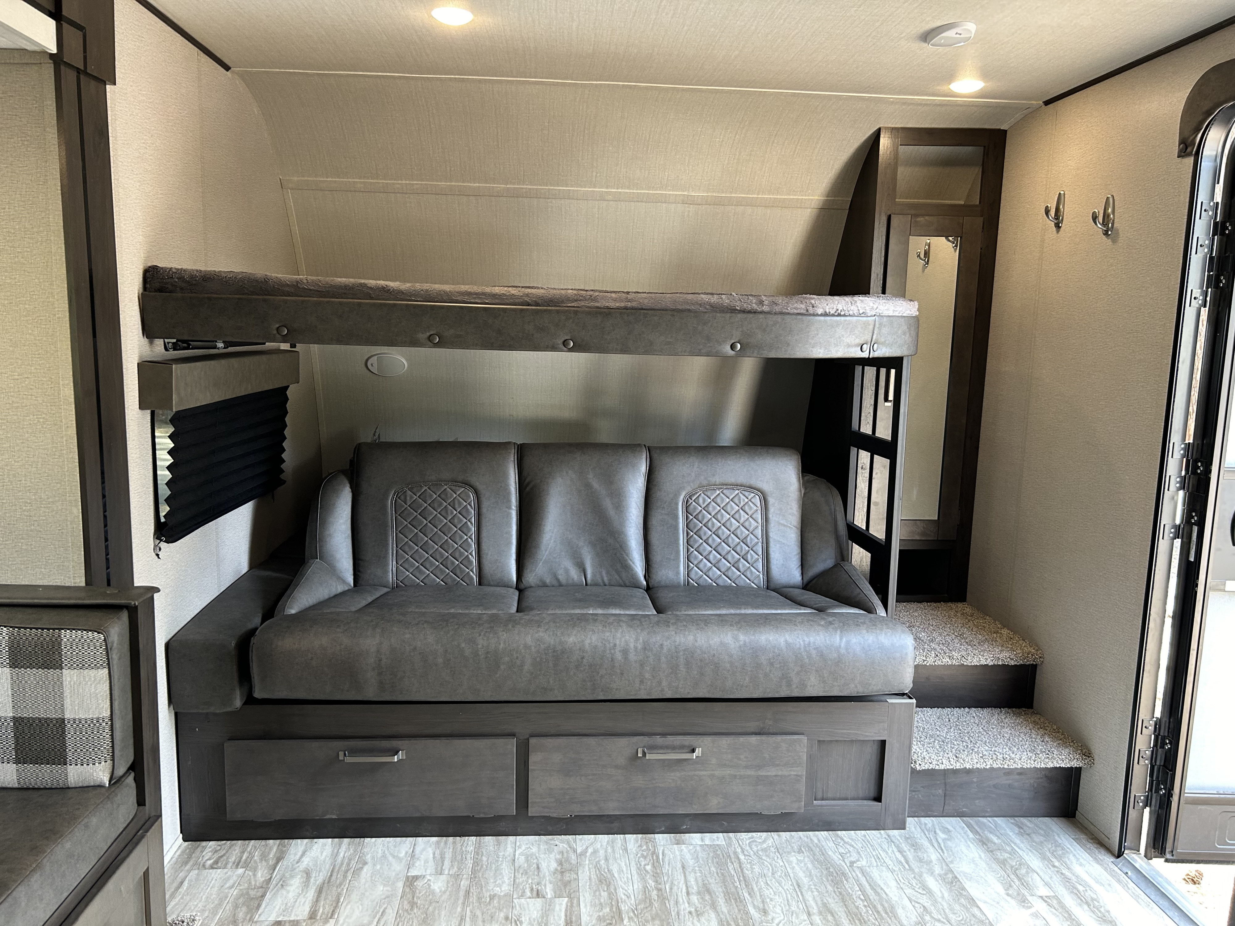 RV rental interior: comfy gray sofa under a bunk bed, with storage drawers, mirror, and hooks. Compact and functional.. Grand Design Transcend Xplor 2023