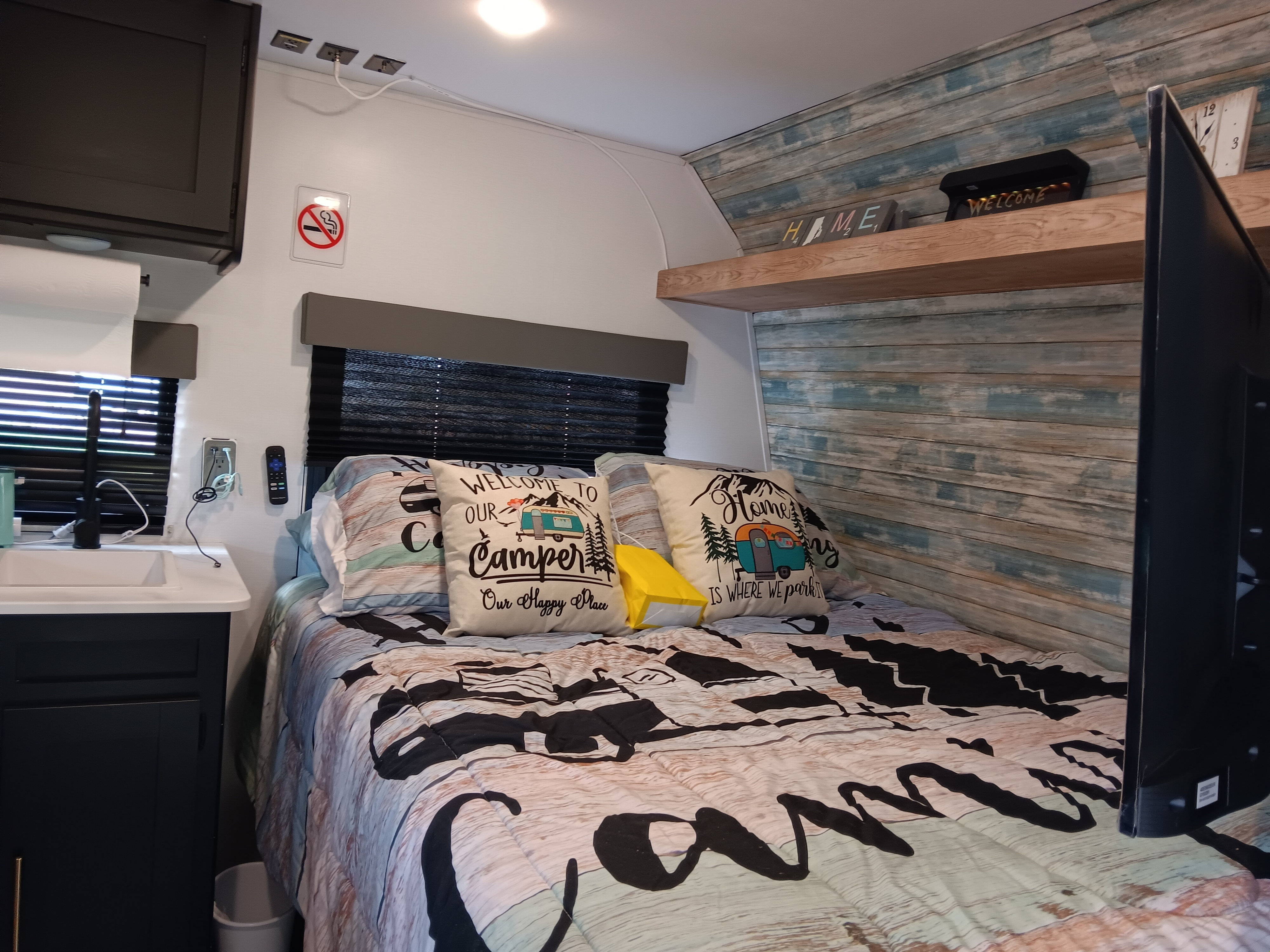 Cozy RV rental interior: bedroom with camping-themed bedding, a comfy bed, small sink, and decorative shelves.. Keystone RV Springdale 2022