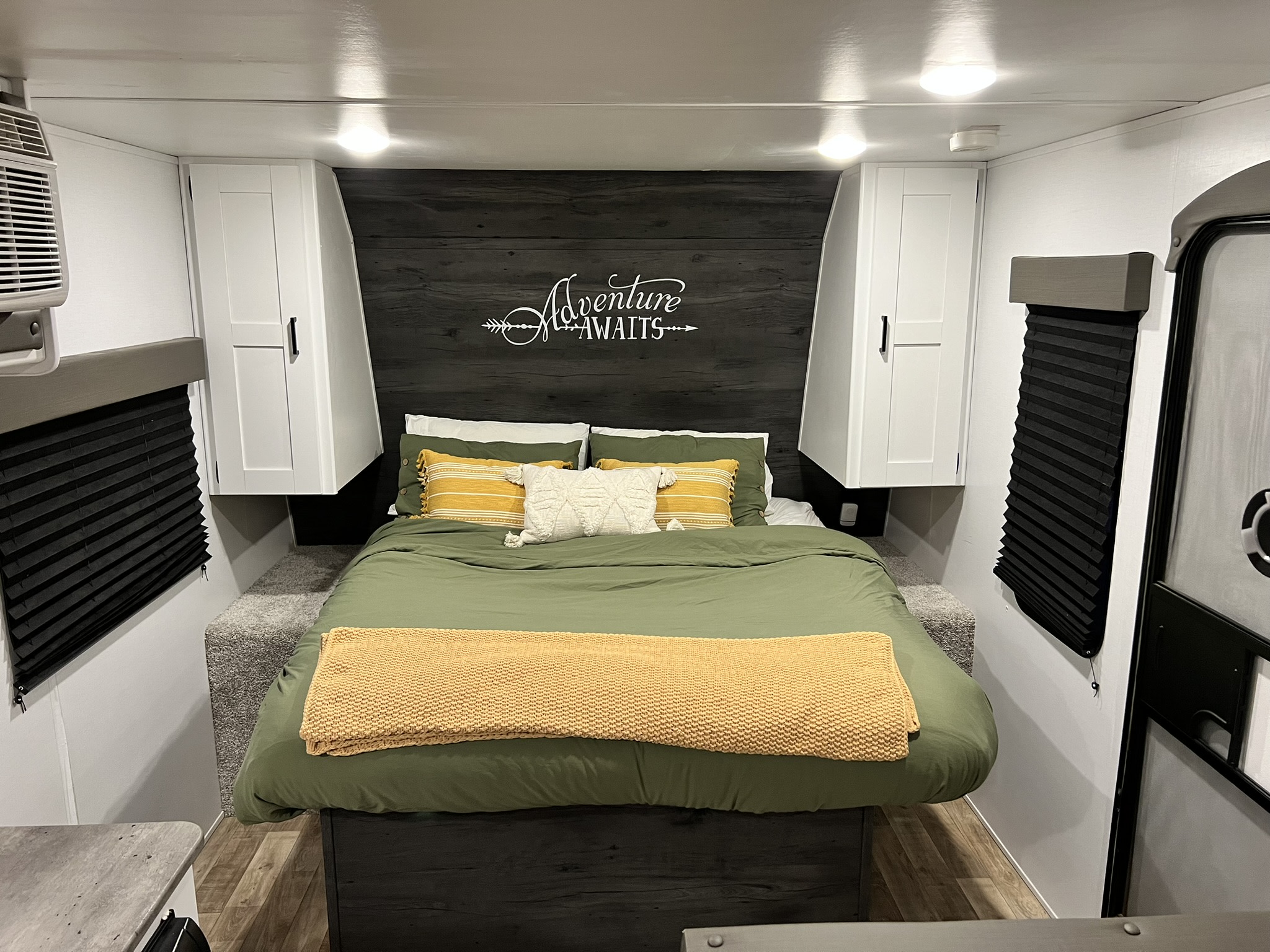 Cozy RV rental bedroom with olive green bedding, 'Adventure Awaits' wall art, and ample storage. Perfect for road trips.. Keystone RV Hideout 2022