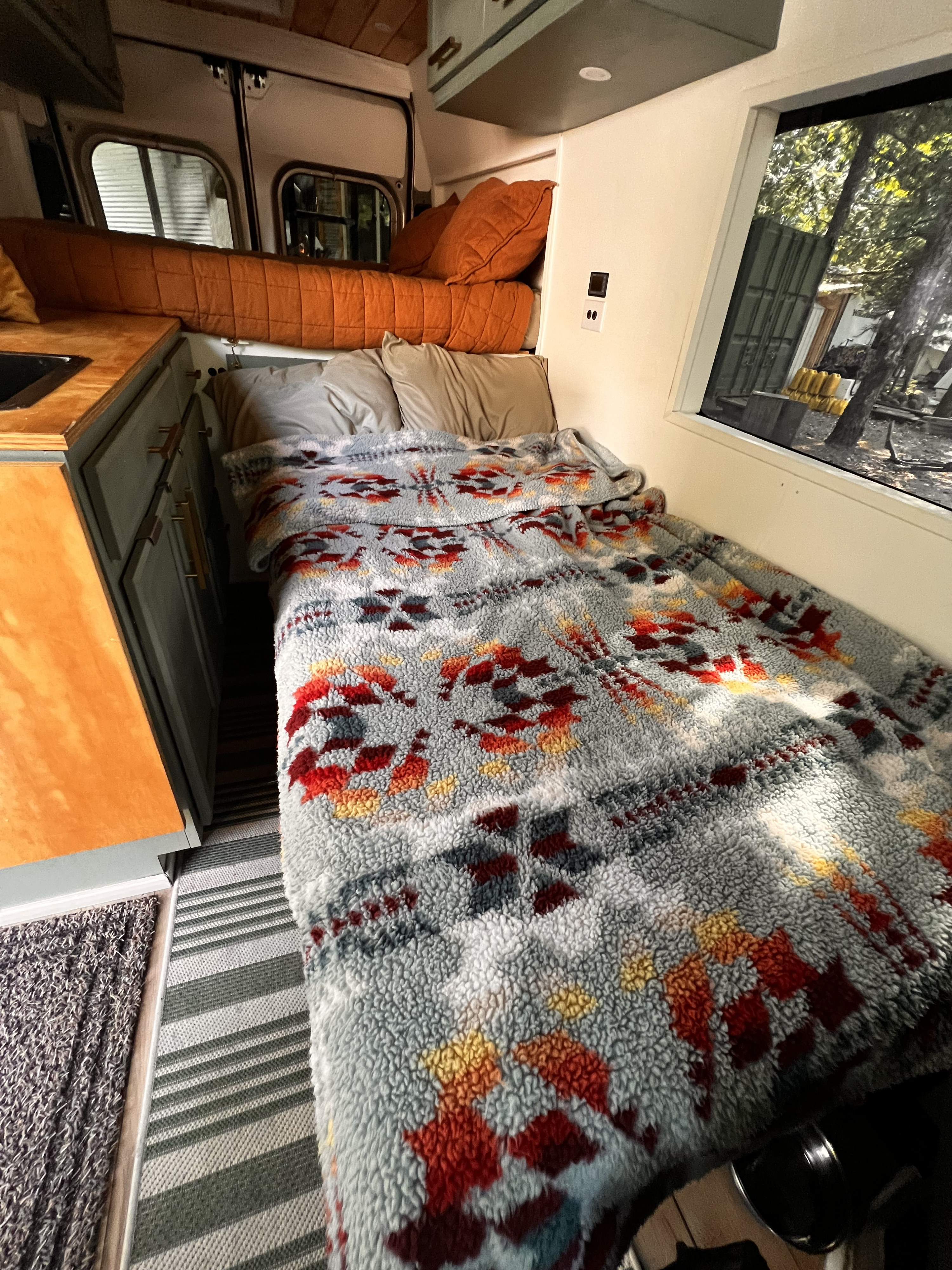 Cozy RV rental interior featuring a comfortable bed with a patterned blanket, kitchen area, and scenic window view.. Dodge Promaster 2500 2023