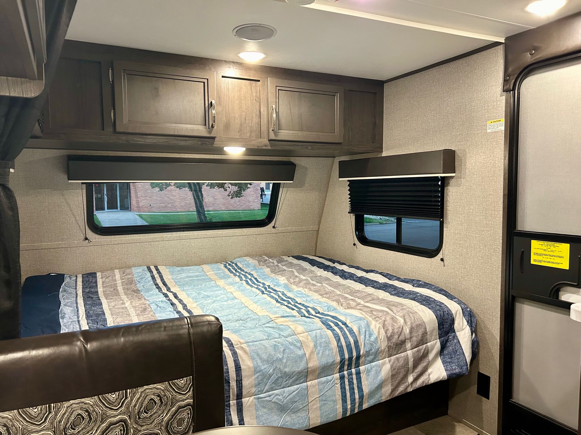Cozy RV rental bedroom with a striped bed, wooden cabinets, and windows revealing outdoor scenery.. Jayco Jay Flight SLX 2020