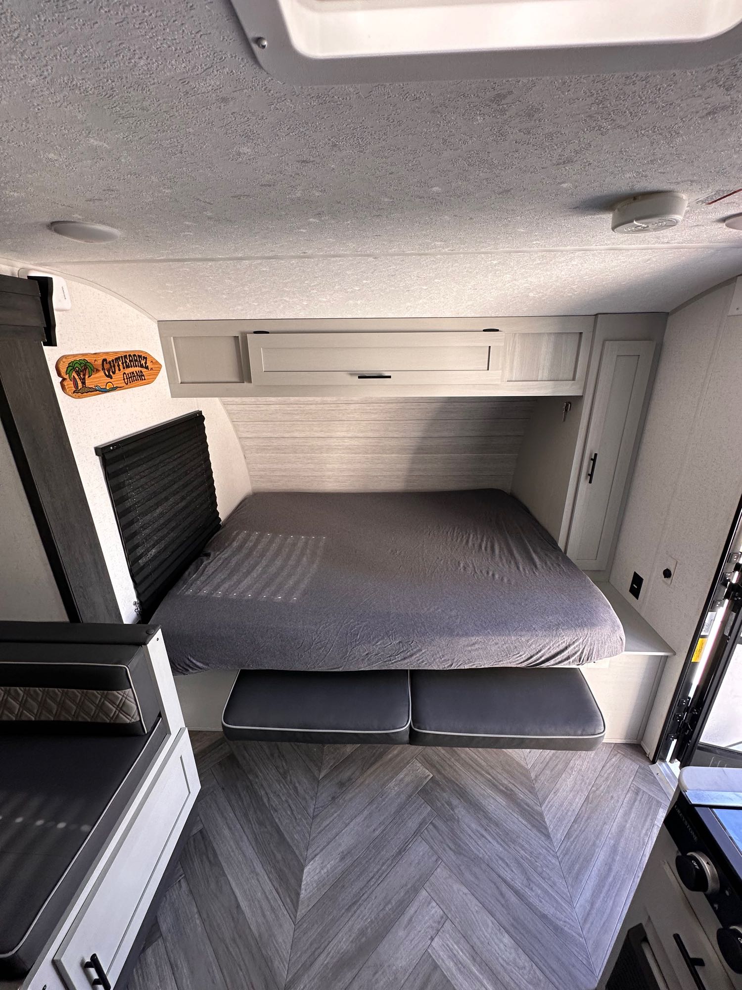 Interior of an rv rental camper: grey bed, sleek overhead cabinets, and a chevron wood floor. A compact, functional space.. Forest River Salem FSX Plantium 2022