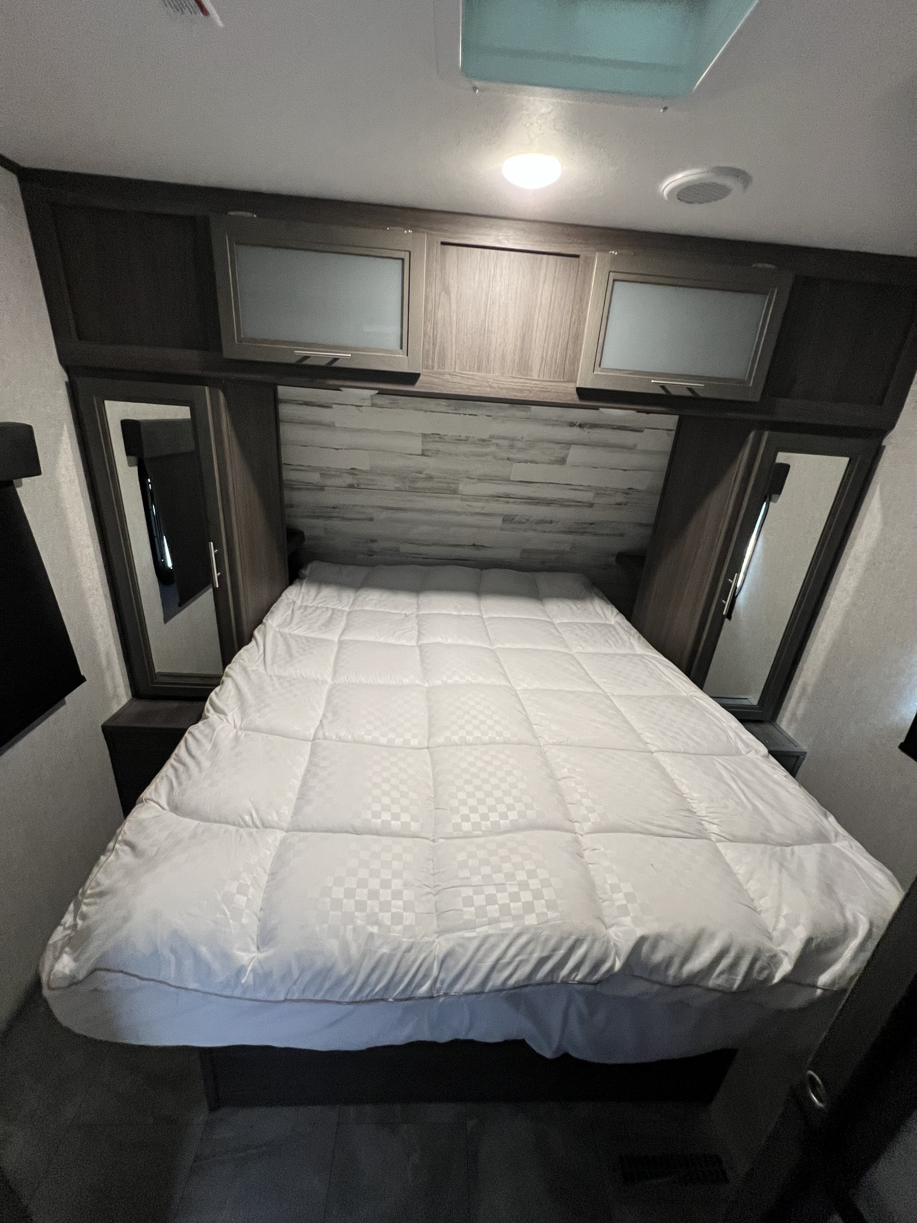 RV rental bedroom: Features a comfortable bed with a white comforter, overhead cabinets, and mirrored wardrobes.. Dutchmen Kodiak Ultra Lite 2021