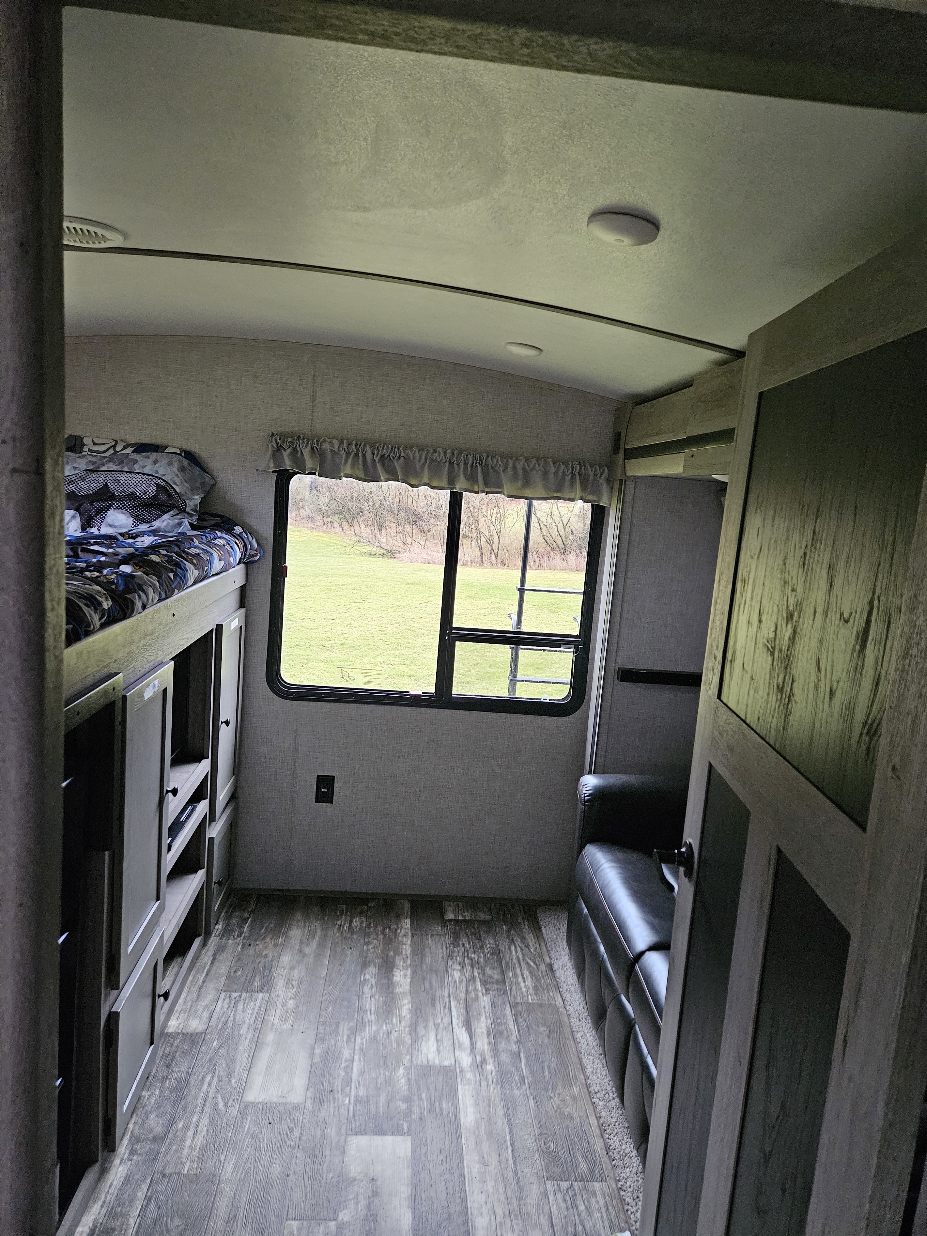 Inside this RV rental: bunk beds on the left, a bright window with a green field view, and a black sofa on the right.. Keystone Outback 2020