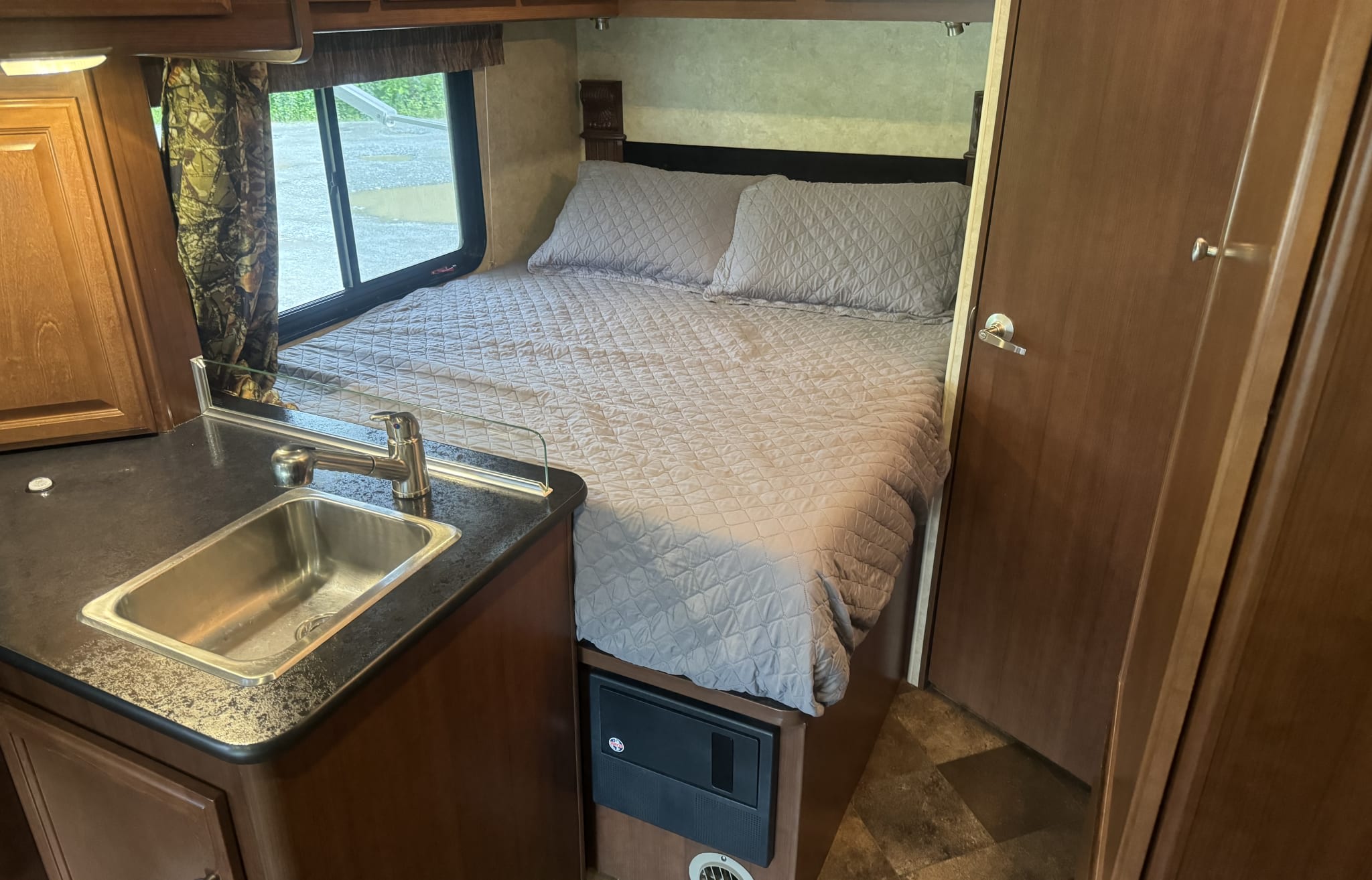 Compact RV rental bedroom with a comfy bed, sink, and window. Ideal for travel and adventure.. Jamboree Searcher 2014
