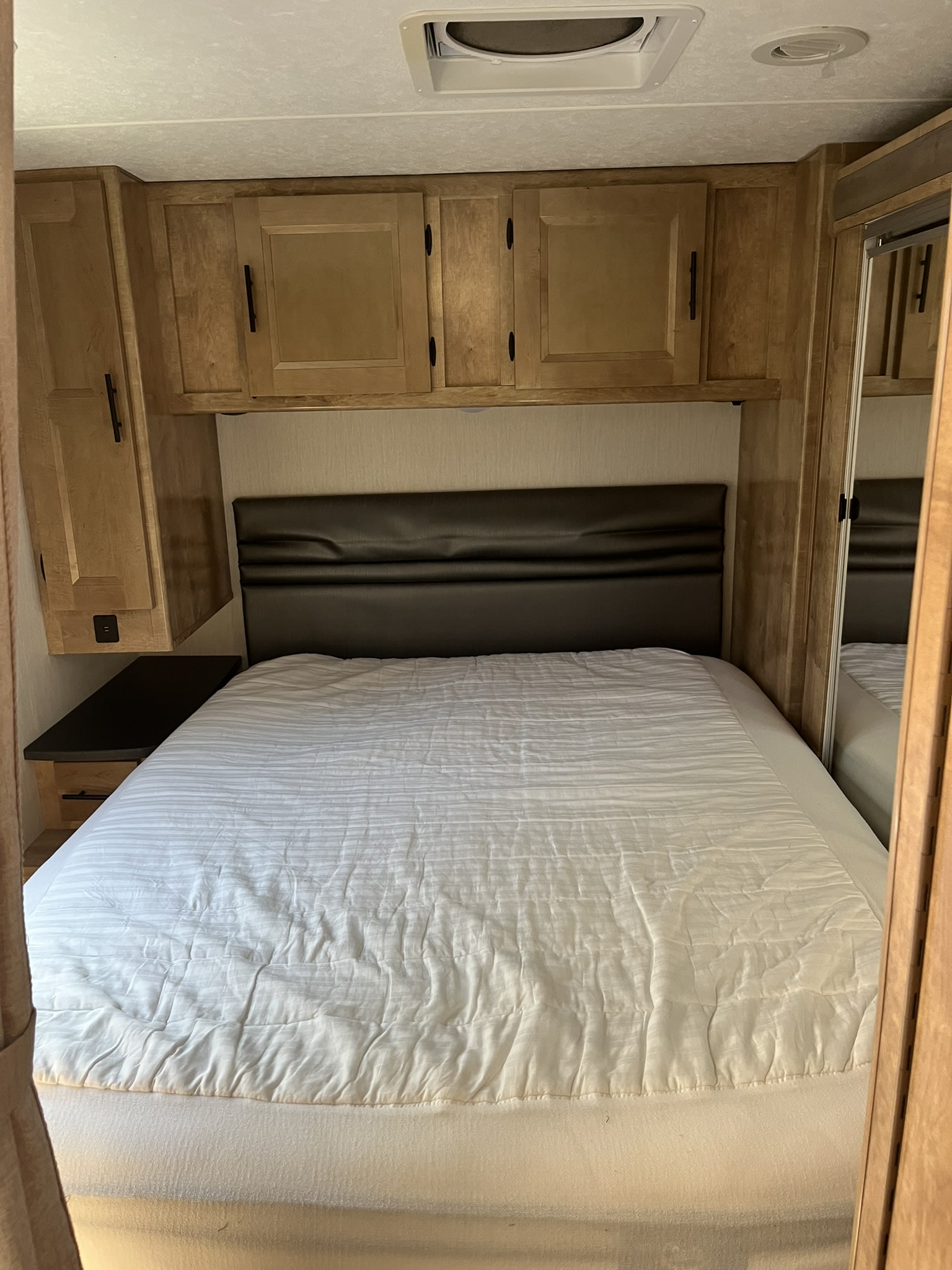 Spacious RV rental bedroom with a comfortable bed, ample wooden storage cabinets, and convenient bedside charging.. Coachmen Leprechaun 2021