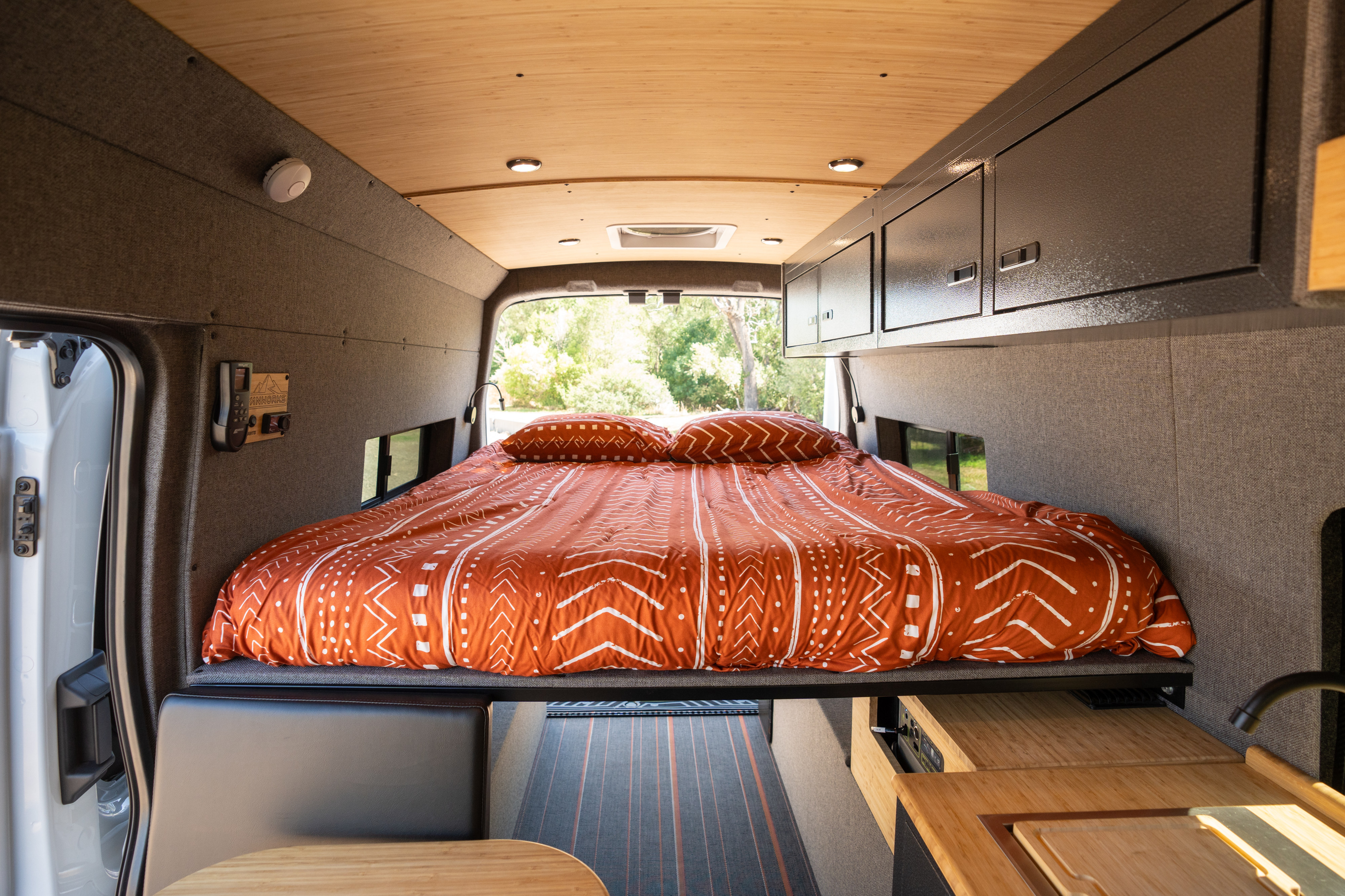 Spacious RV rental interior featuring a cozy bed, wood-paneled ceiling, storage, and a kitchen area.. Mercedes-Benz Sprinter 2024