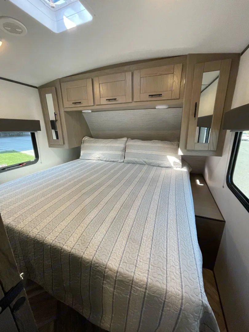 Inside an RV rental: a bright bedroom with a queen bed, overhead cabinets, and side mirrors. Perfect for travel comfort.. Cruiser RV Shadow Cruiser 2022