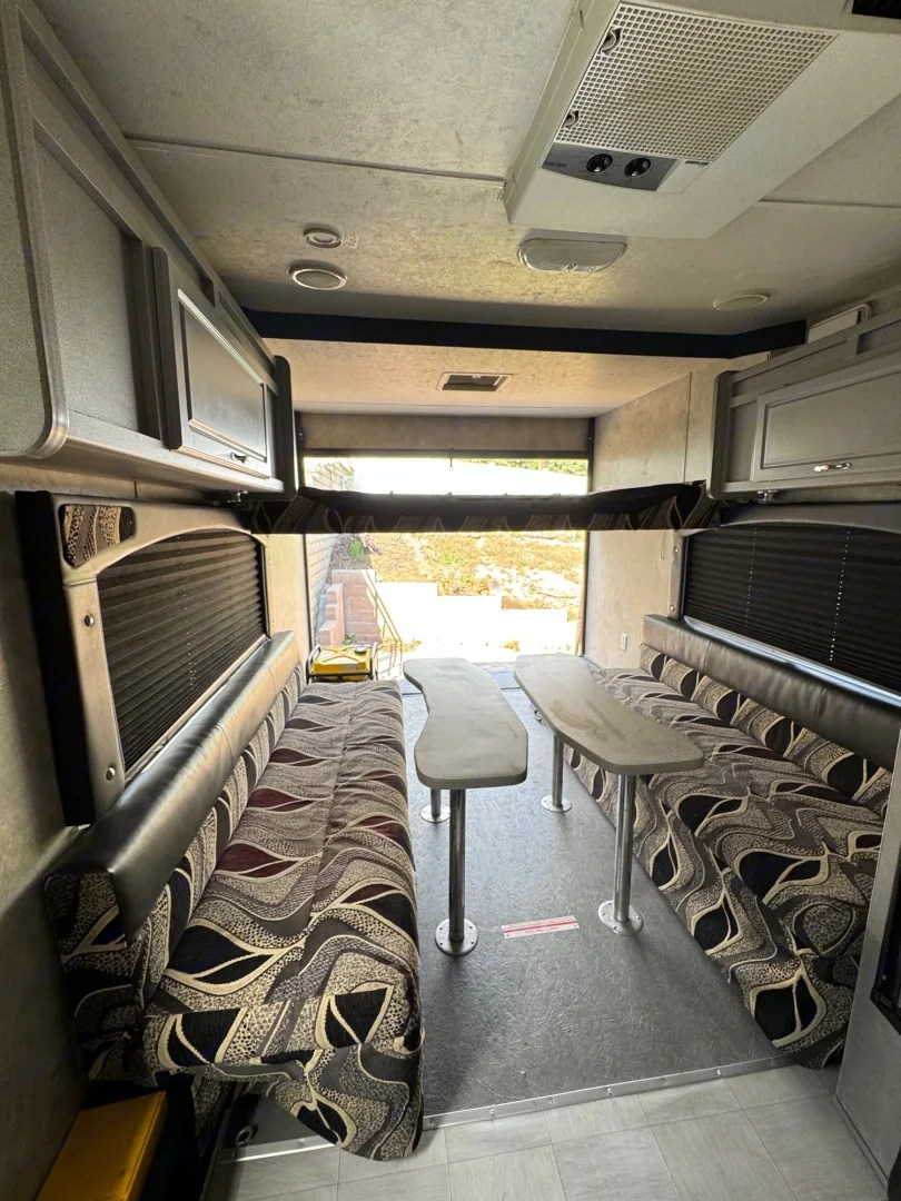 Inside an RV rental: a flexible living area with comfortable patterned benches, tables, and a stowed overhead bunk.. Weekend Warrior 1800sxfk 2009
