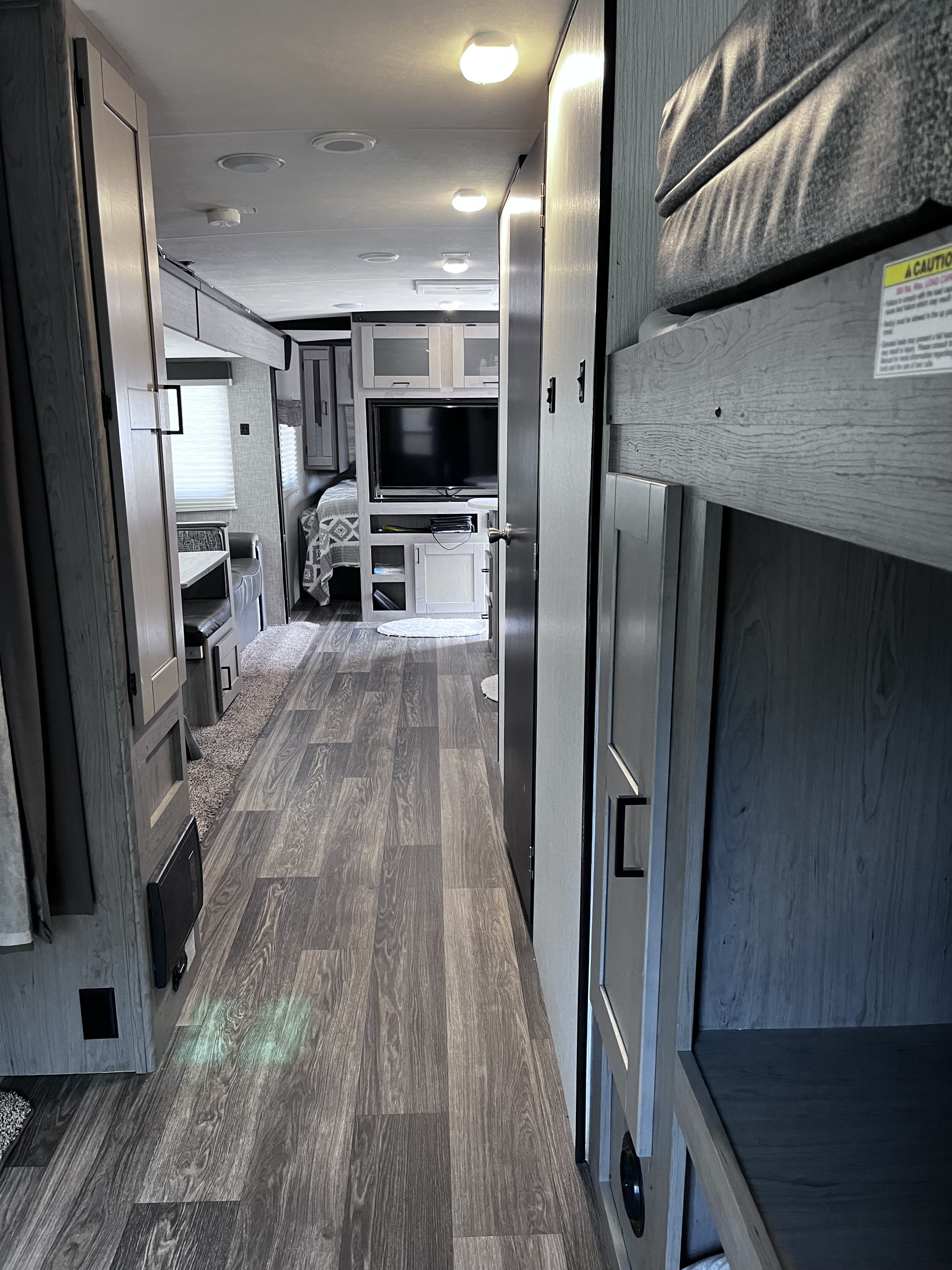 RV rental interior: A bright, modern hallway with wood-look floors, showing bunk beds, a dinette, and bedroom area.. Heartland RVs Mallard 2021