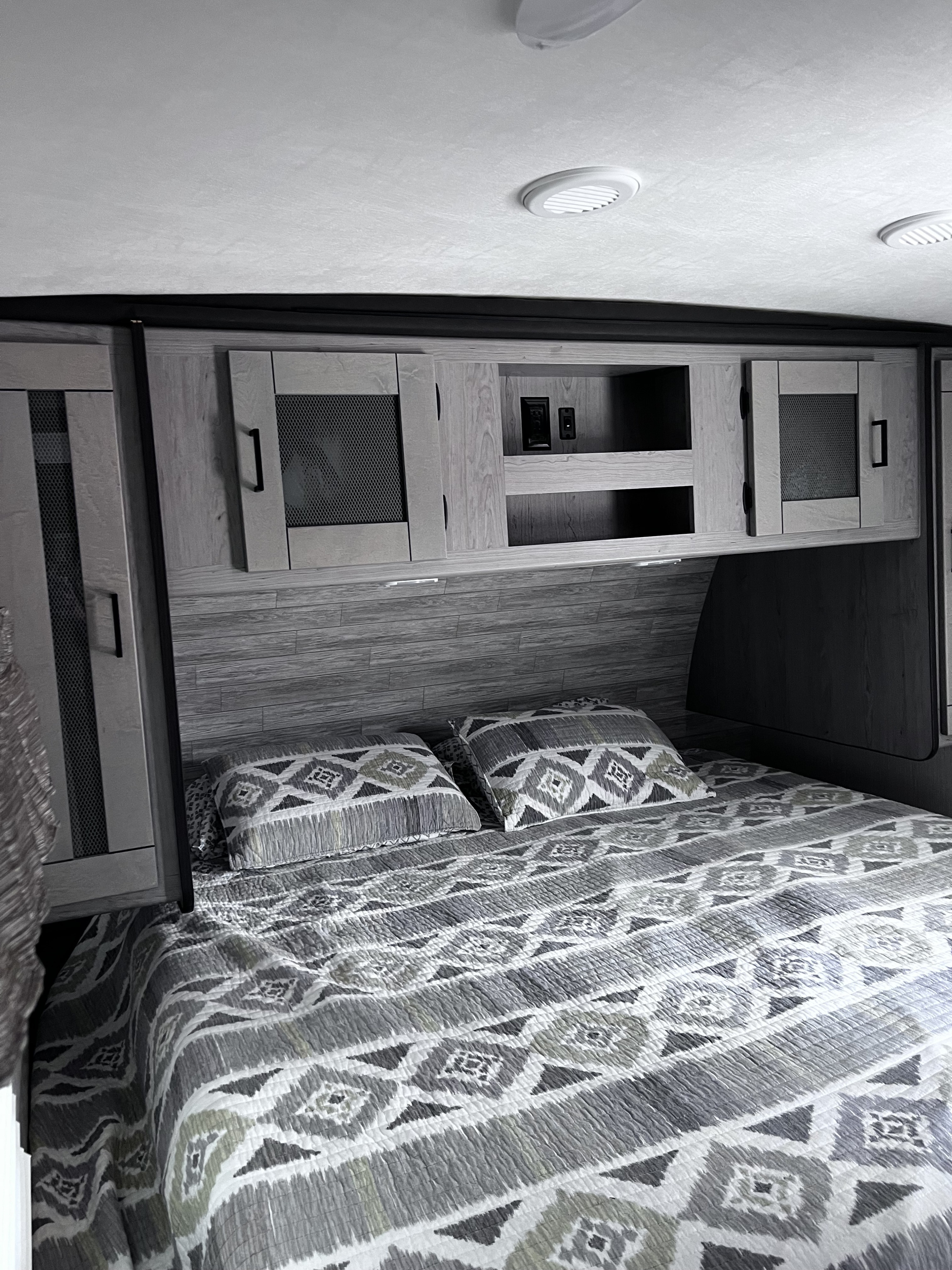 RV rental bedroom: comfy bed with patterned quilt, pillows, and practical overhead cabinets with storage.. Heartland RVs Mallard 2021
