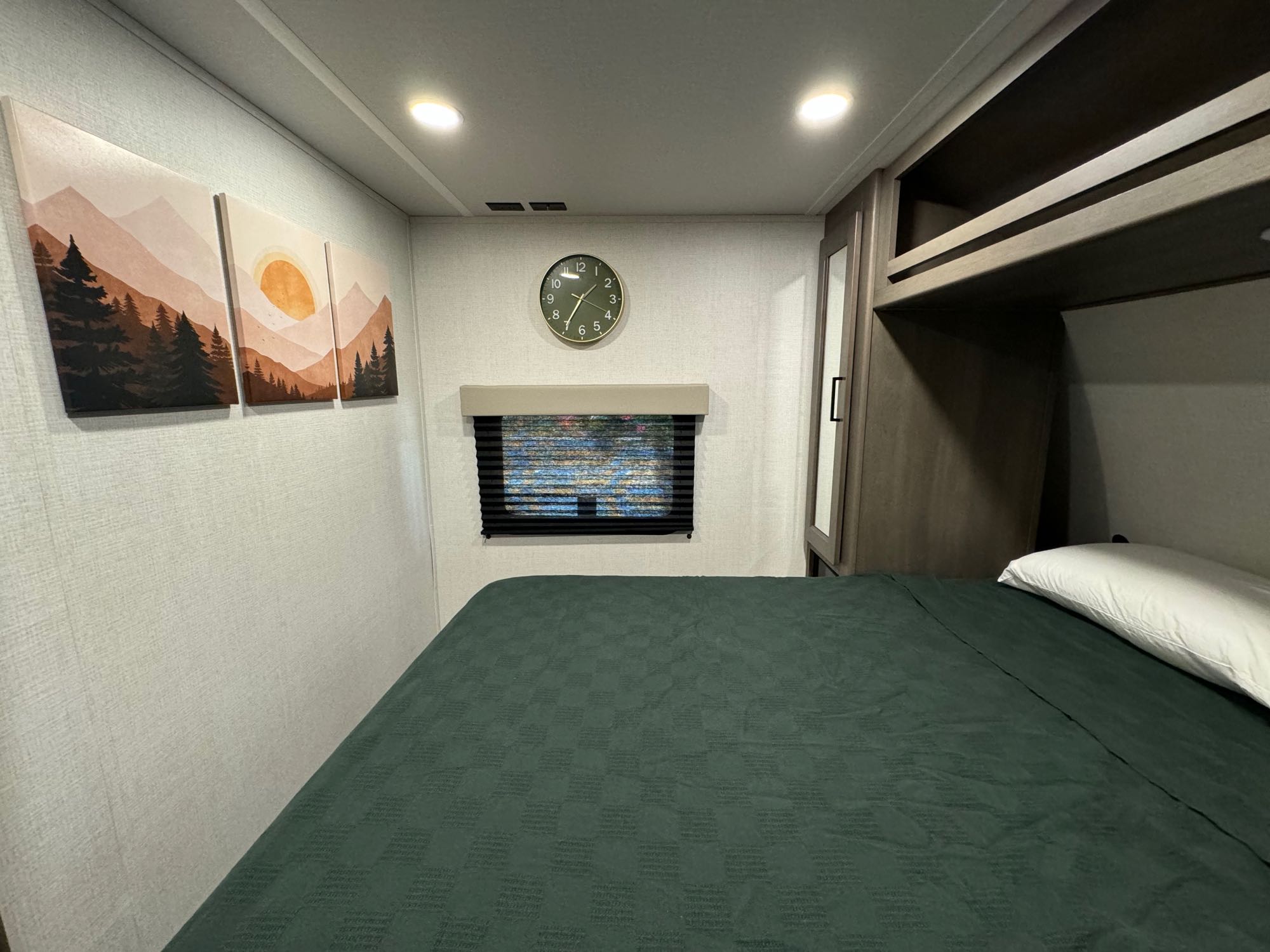 Cozy RV rental bedroom featuring a comfortable bed, nature-themed wall art, a clock, and practical storage.. Grand Design Transcend Xplor 26BHX 2024
