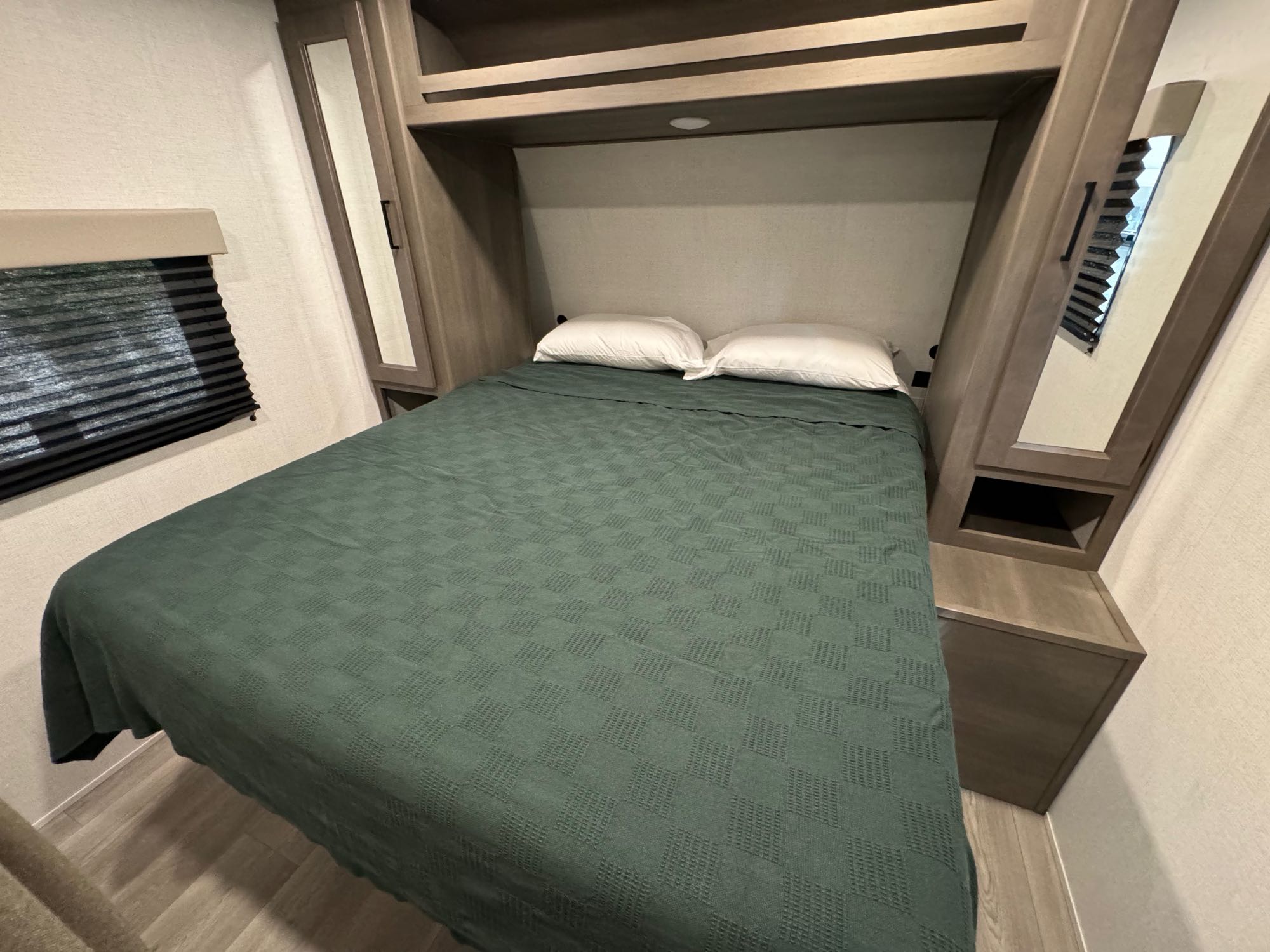 Step into comfort in this RV rental bedroom: a double bed with green spread, overhead & side storage.. Grand Design Transcend Xplor 26BHX 2024