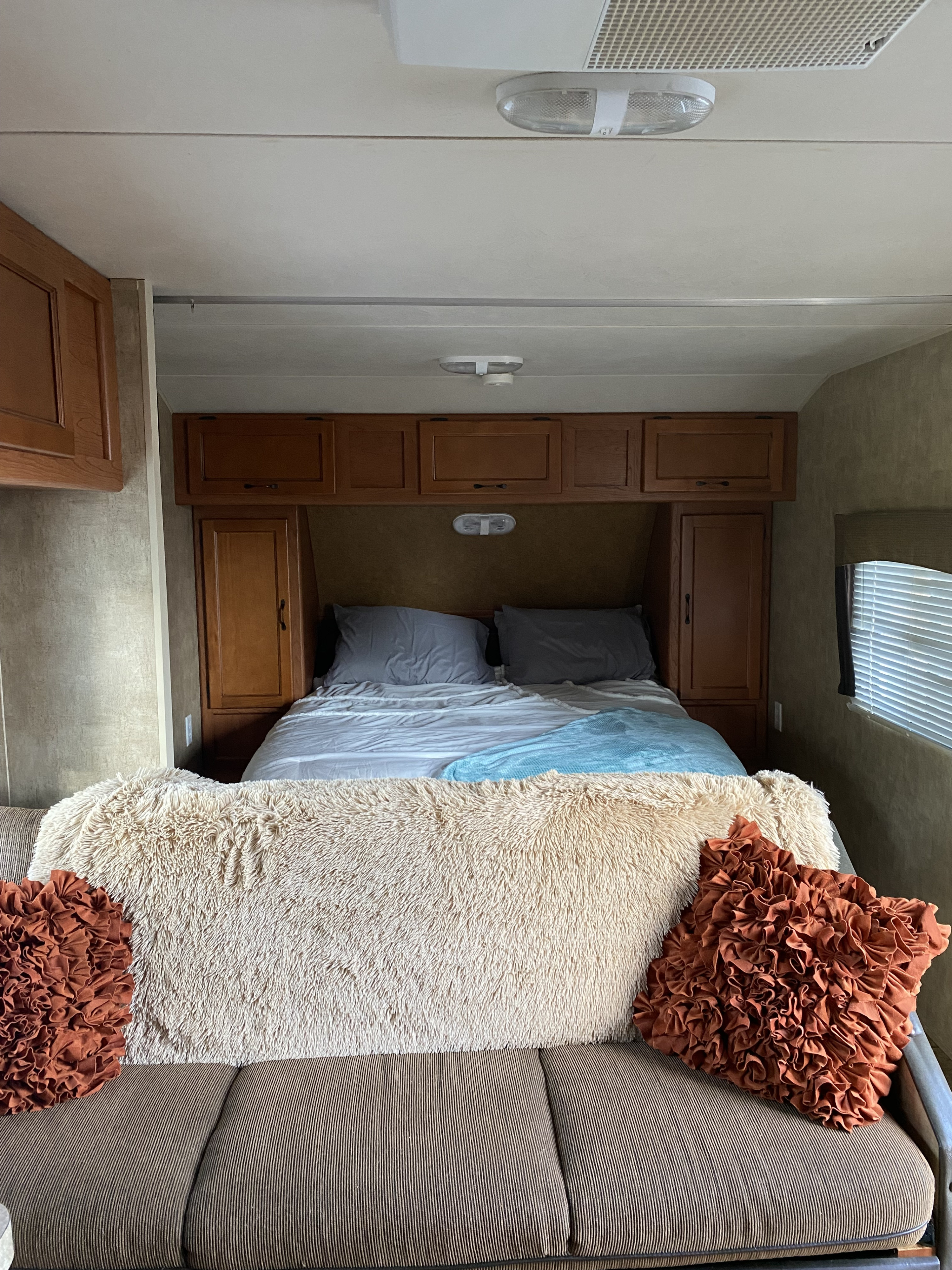 Cozy RV rental interior with a bed, wood cabinets, and a sofa adorned with a fluffy blanket and ruffled pillows.. Forest River Cherokee Grey Wolf 2012