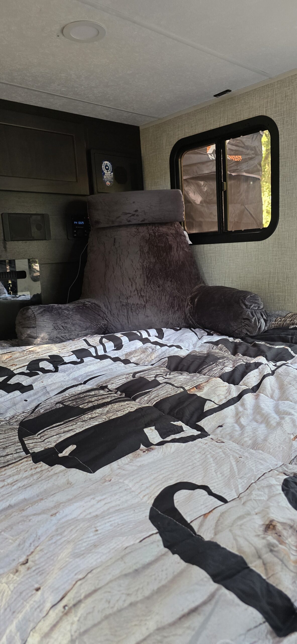 Relaxing RV rental bedroom: A bed with a wood-patterned duvet, a soft gray backrest pillow, and a small window view.. Braxton Creek Bushwhacker 2024
