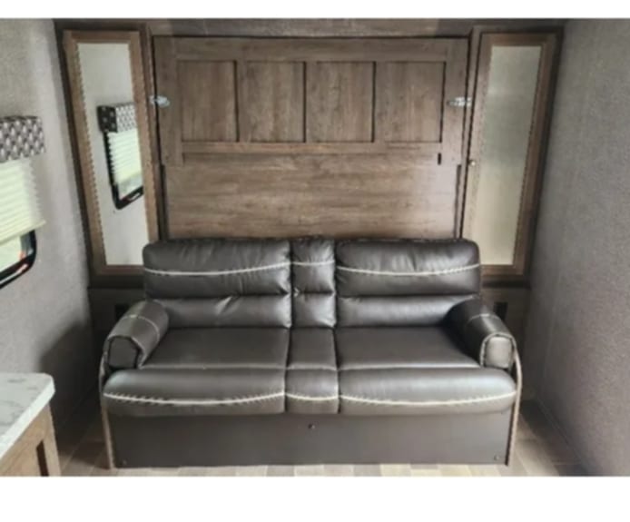 RV rental living area: Dark brown sofa beneath a folded murphy bed. Efficient space usage.. Dutchmen Coleman Light LX 2020
