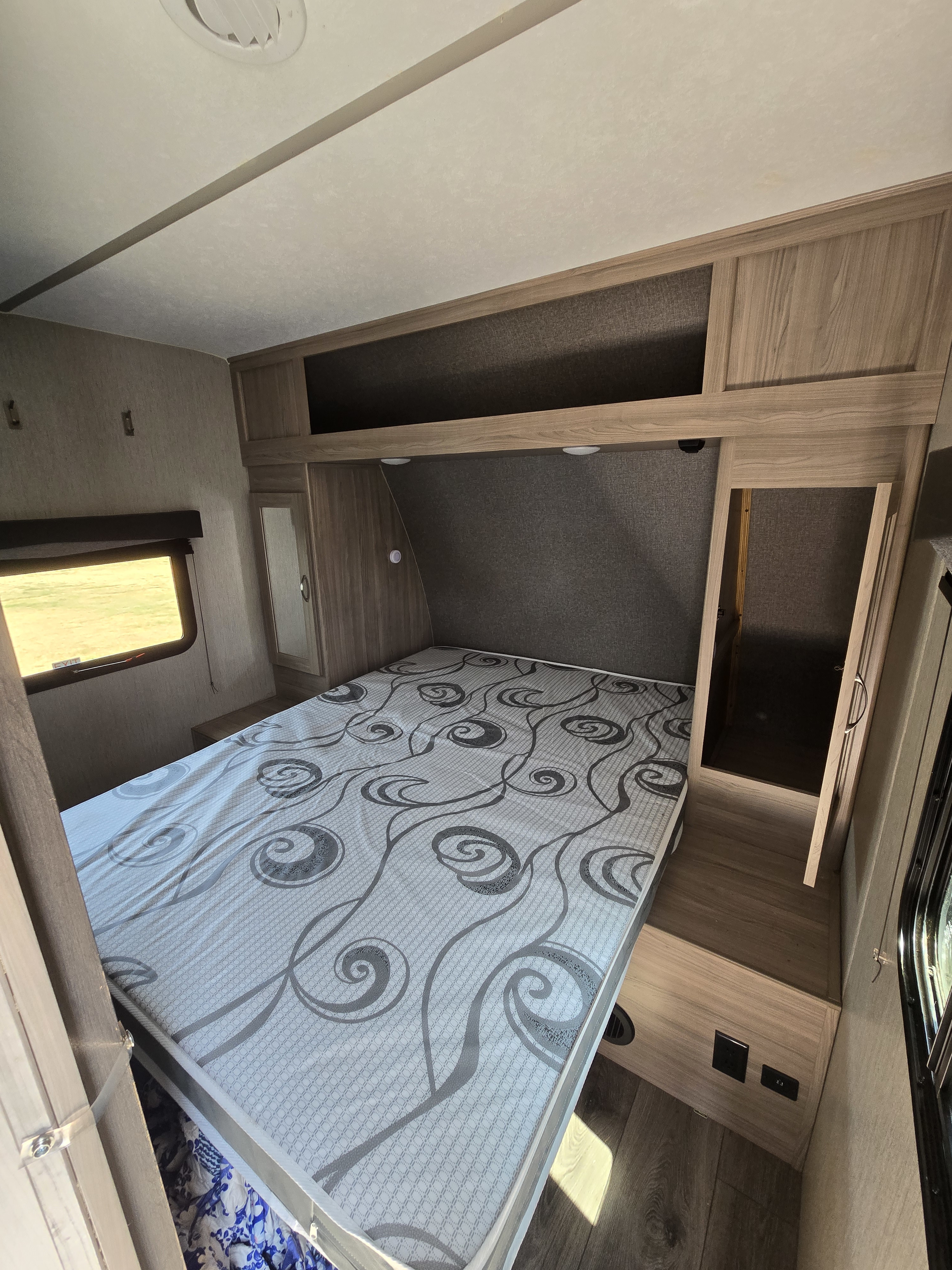 RV rental bedroom featuring a patterned bed, modern cabinets, and a side window, offering a comfortable stay.. Coachmen Freedom Express 2022