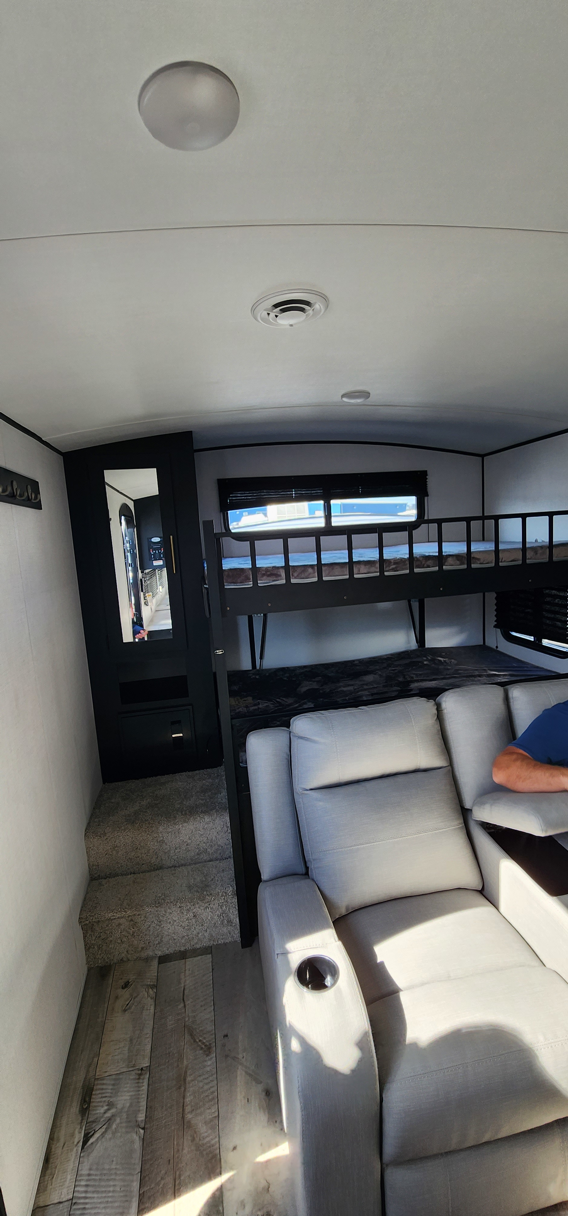 Spacious RV rental interior featuring a light grey reclining sofa, bunk beds, and stairs leading to an upper level.. Keystone RV Springdale 2023
