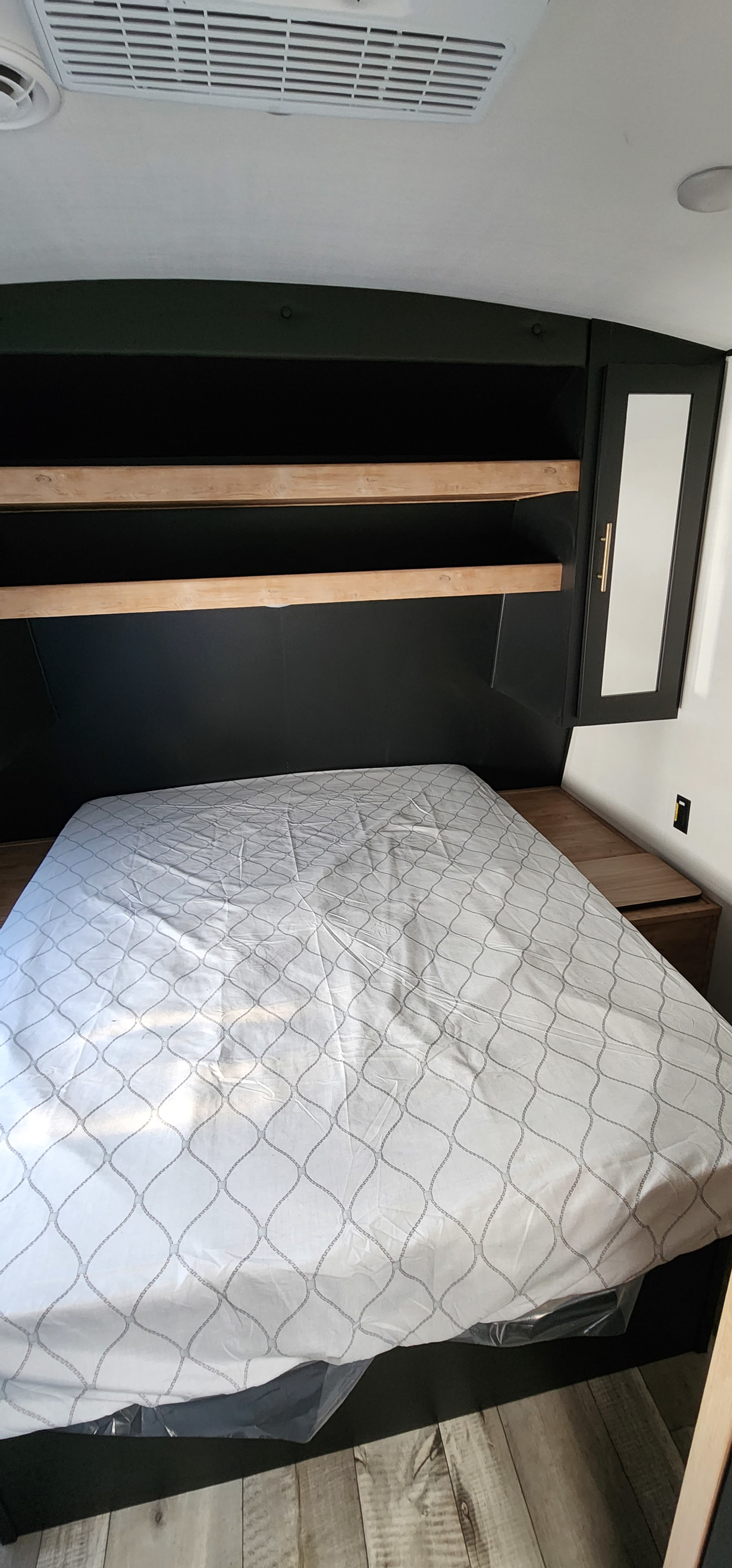 Modern RV rental bedroom featuring a queen bed, built-in overhead shelving, and AC unit.. Keystone RV Springdale 2023