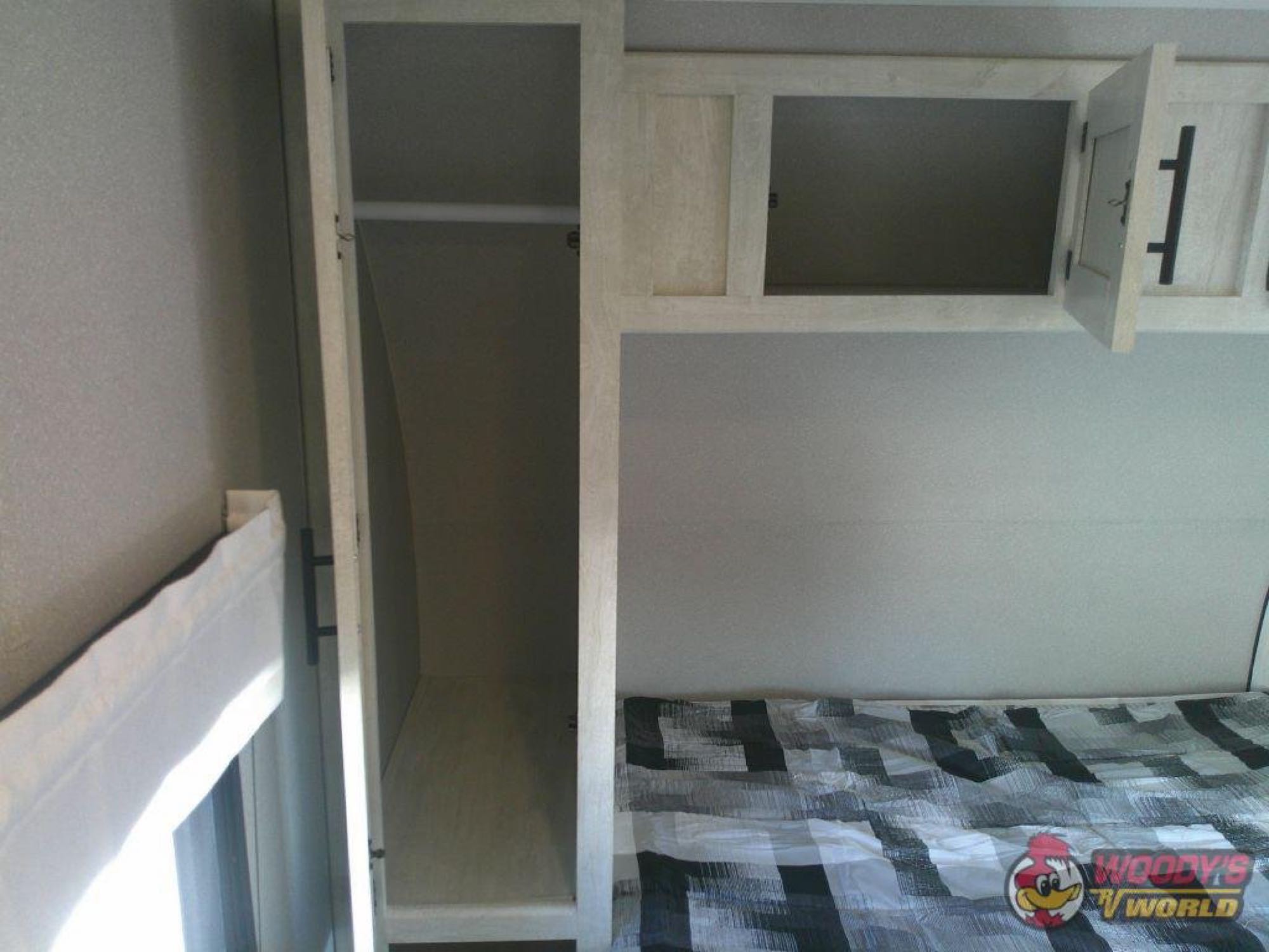 RV rental bedroom: closet on left, bed with modern comforter, and overhead cabinets (one open) for storage.. Forest River Shasta 2022