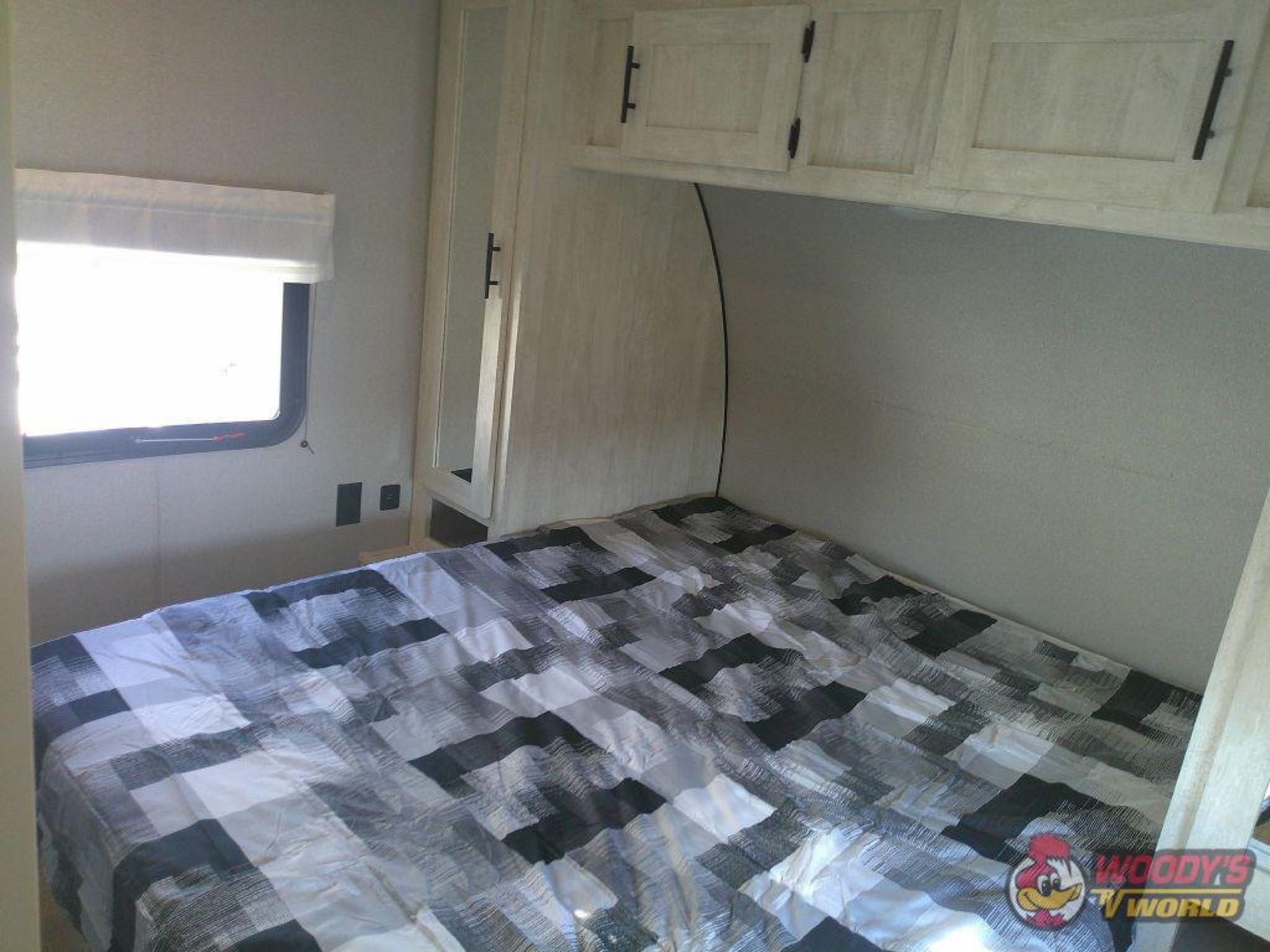 Cozy RV rental bedroom features a bed with a modern checkered comforter, light wood cabinets, and a window.. Forest River Shasta 2022