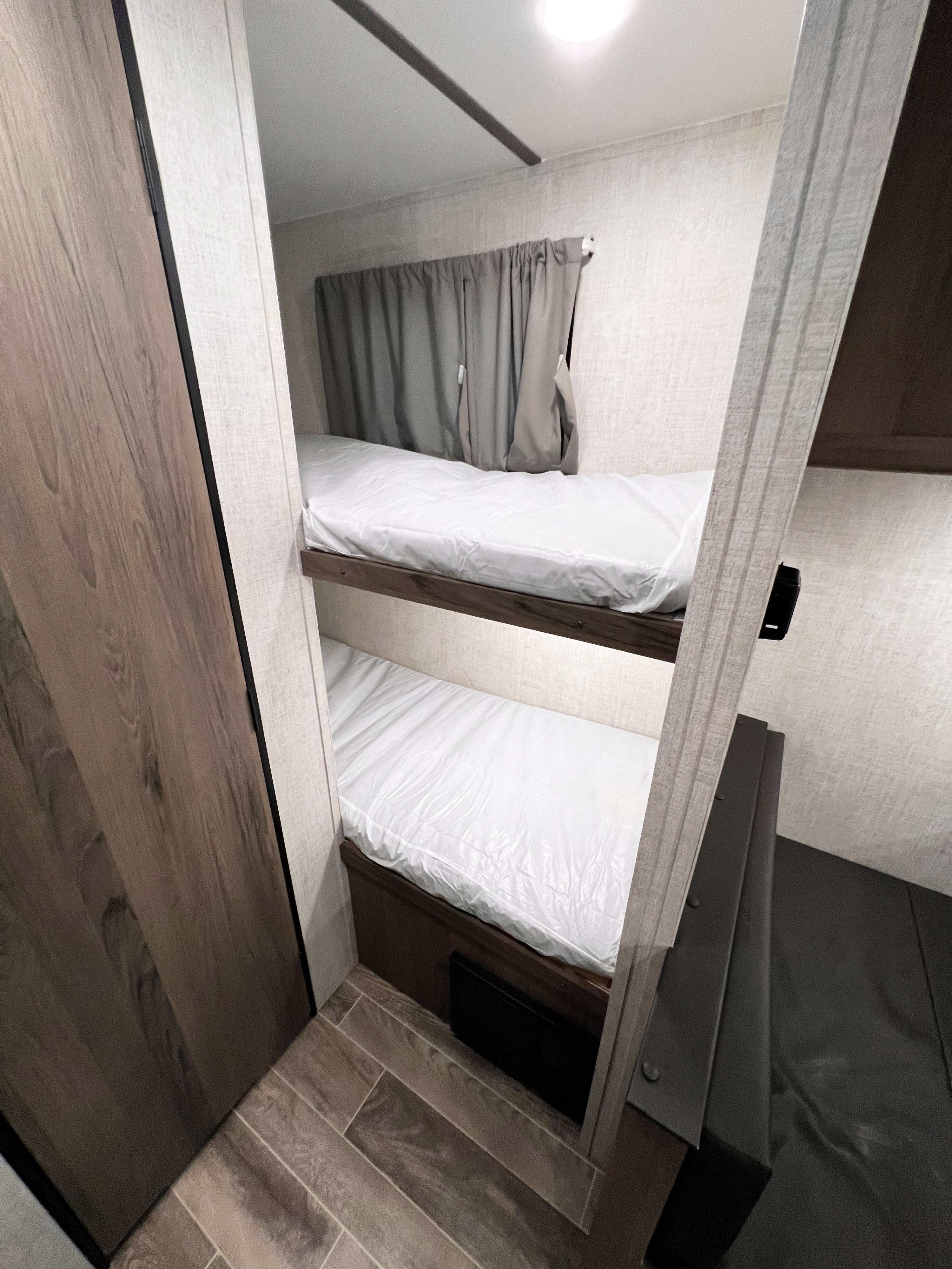 RV rental bunk beds: a clean, compact interior with new plastic-wrapped mattresses, wood trim, and textured walls.. Gulf Stream Ameri-Lite 2022