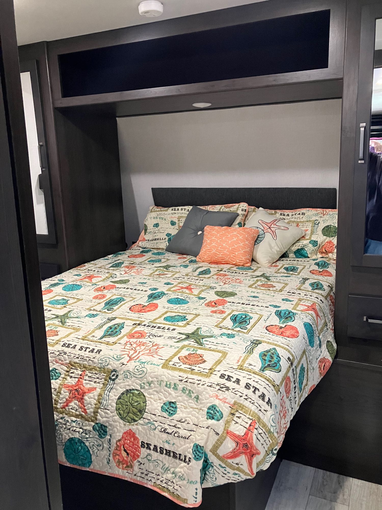 Cozy RV rental bedroom featuring a sea-themed bed with colorful quilt and pillows, surrounded by dark built-in cabinetry.. Grand Design Momentum Toy Hauler 2024