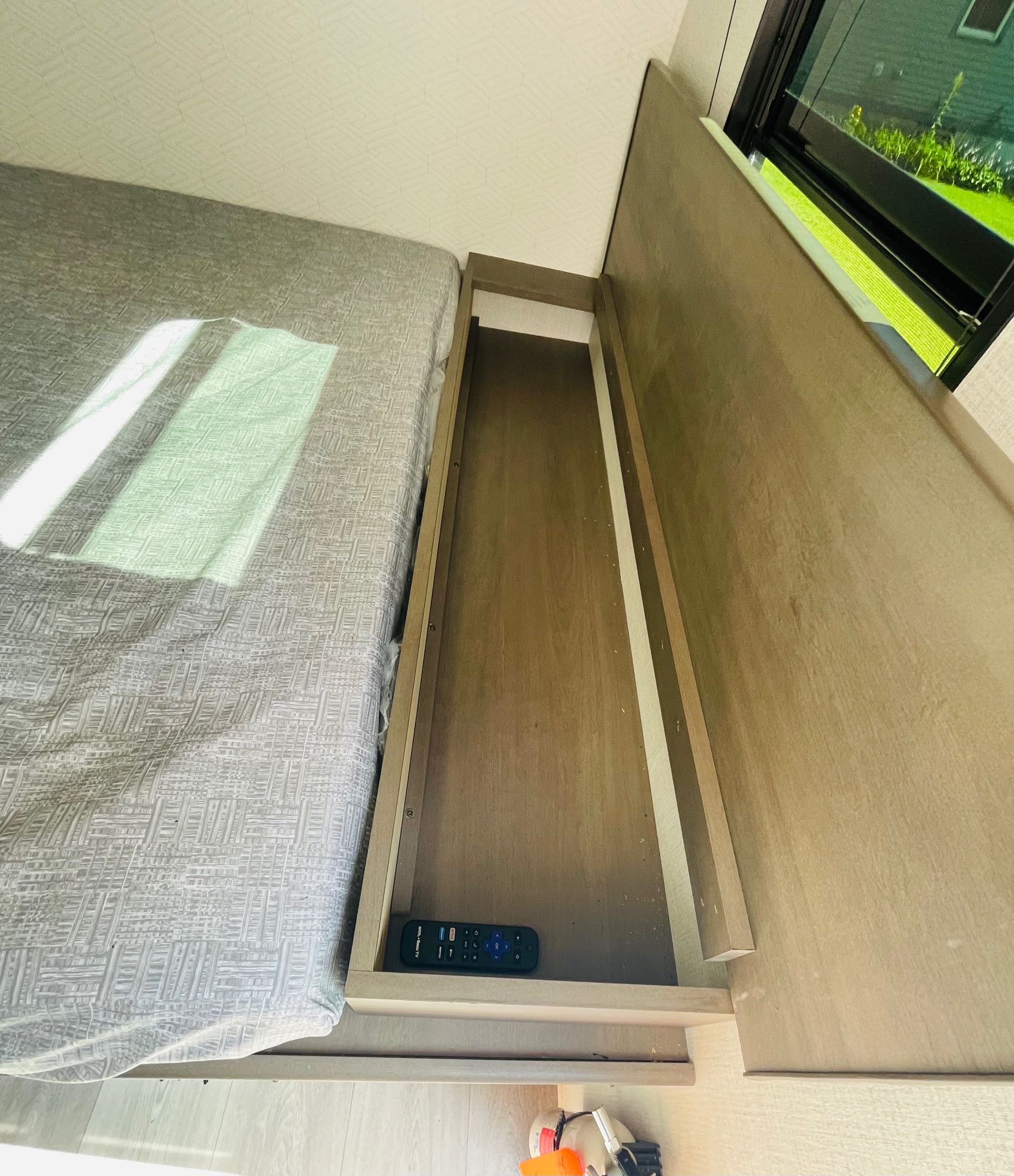RV rental bedroom with compact bed, open storage cubby holding a remote, and window view. Ideal travel space.. Grand Design Transcend One 151BH 2025