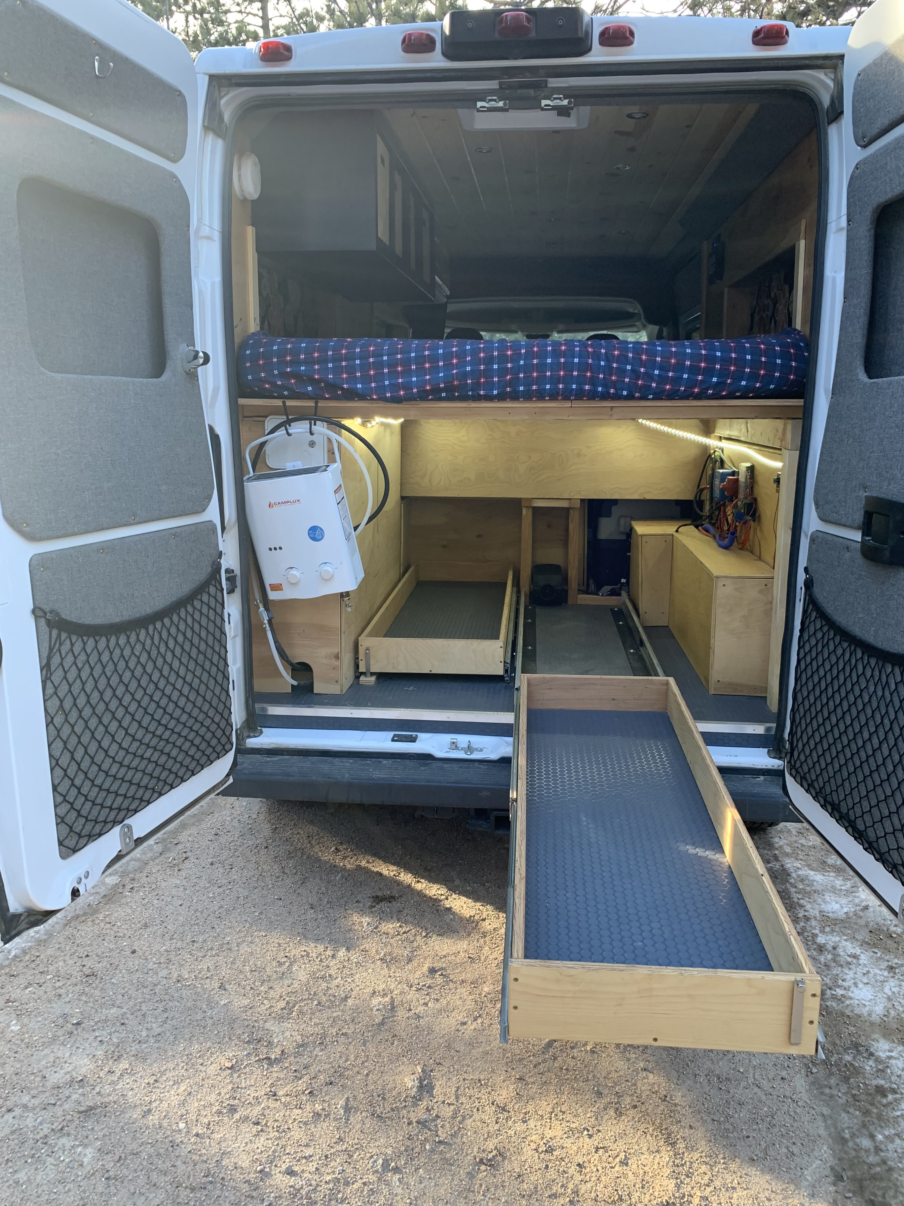 This RV rental shows a well-organized camper van interior with a bed, water heater, pull-out storage, and custom wood cabinetry.. Dodge Promaster 2500 2017