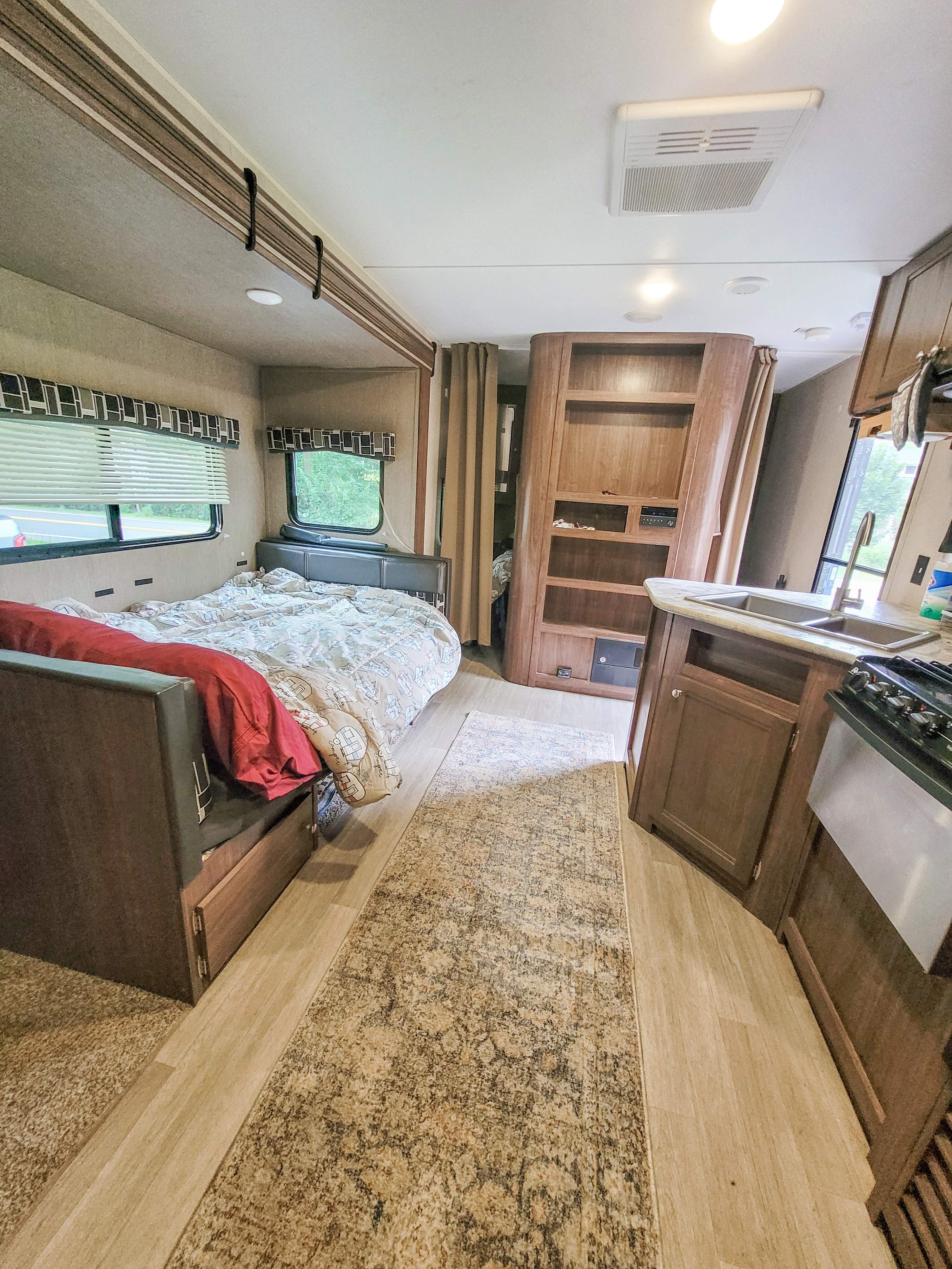 Spacious RV rental interior featuring a cozy bedroom area, a built-in shelving unit, and a compact kitchen with sink and stove.. Dutchmen Coleman Lantern LT 2017