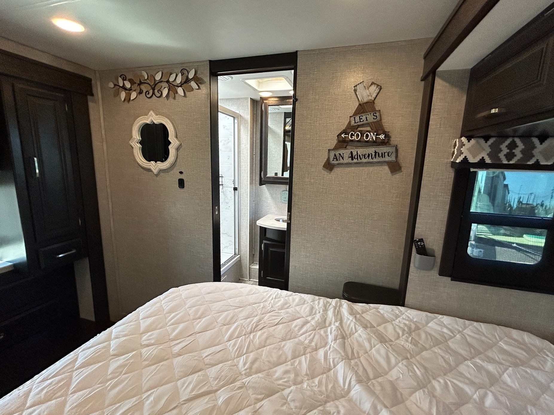 This RV rental features a cozy bedroom with white bedding, an ensuite bathroom, and adventure decor, ready for travel.. Entegra Coach Vision XL 2022
