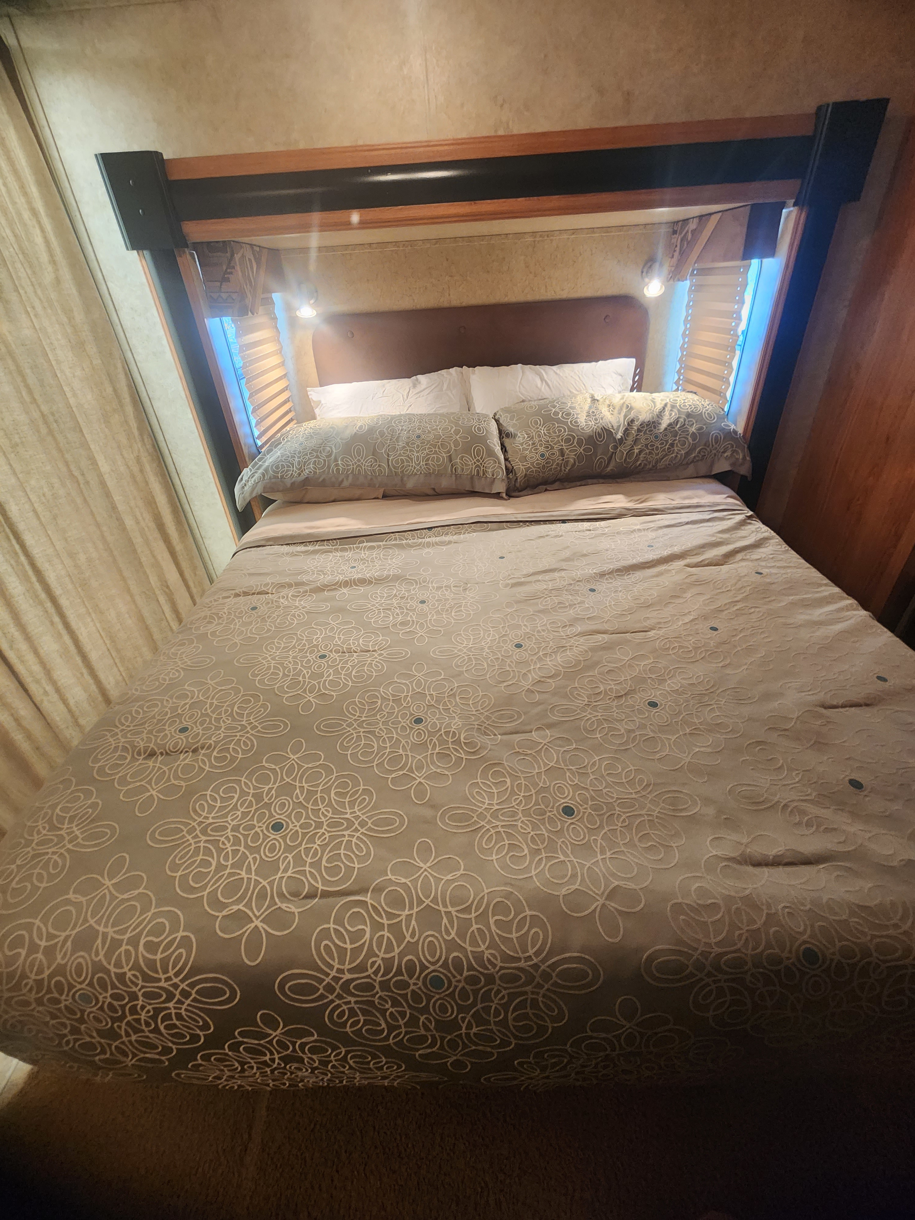A cozy RV rental bedroom features a neatly made bed with patterned bedding, pillows, and bright reading lights illuminating the headboard.. Jayco Recon Toy Hauler 2008
