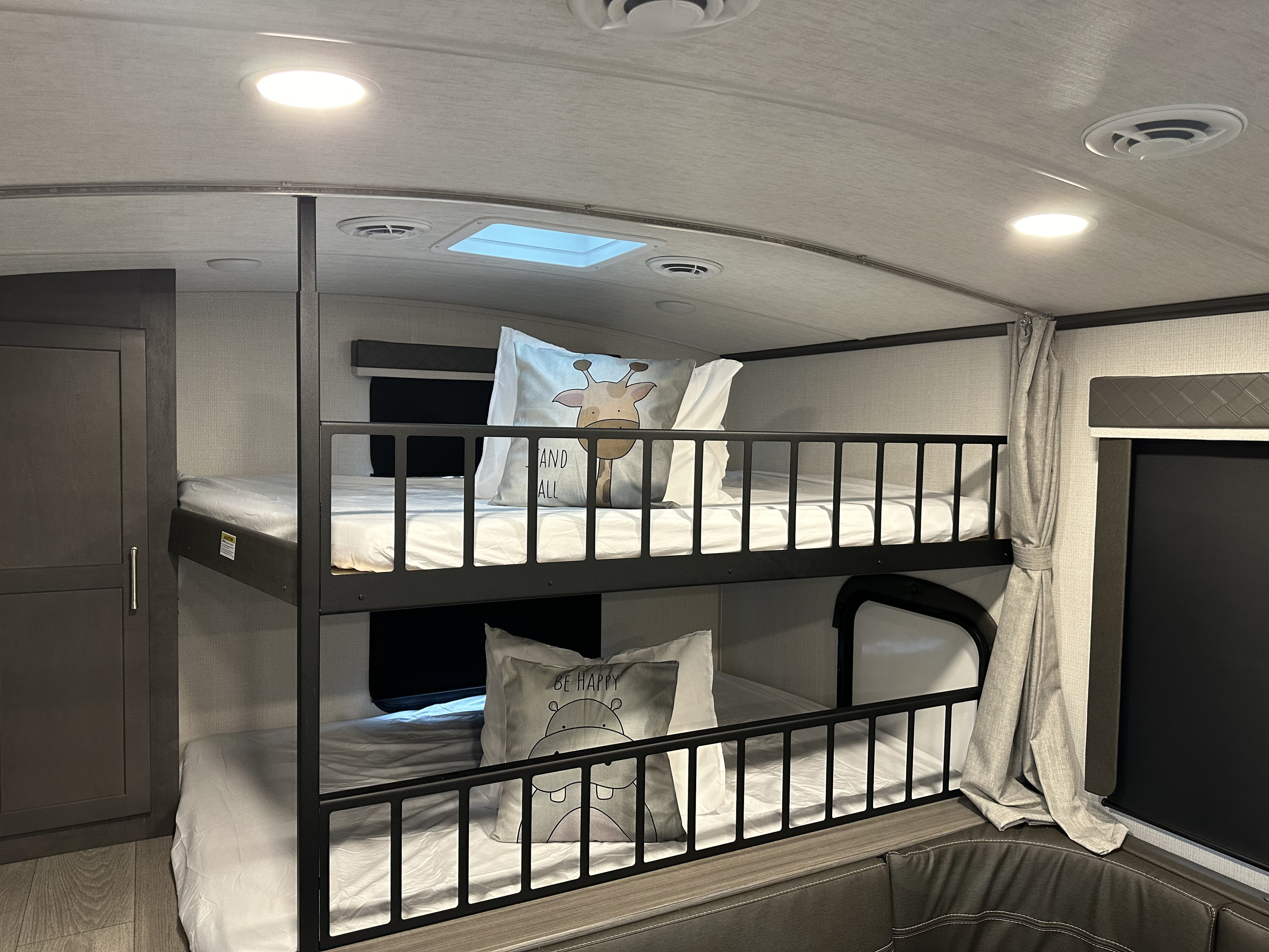 Interior of an RV rental showing a set of clean, modern bunk beds with decorative pillows, ceiling lights, and storage.. Keystone RV Cougar 2024