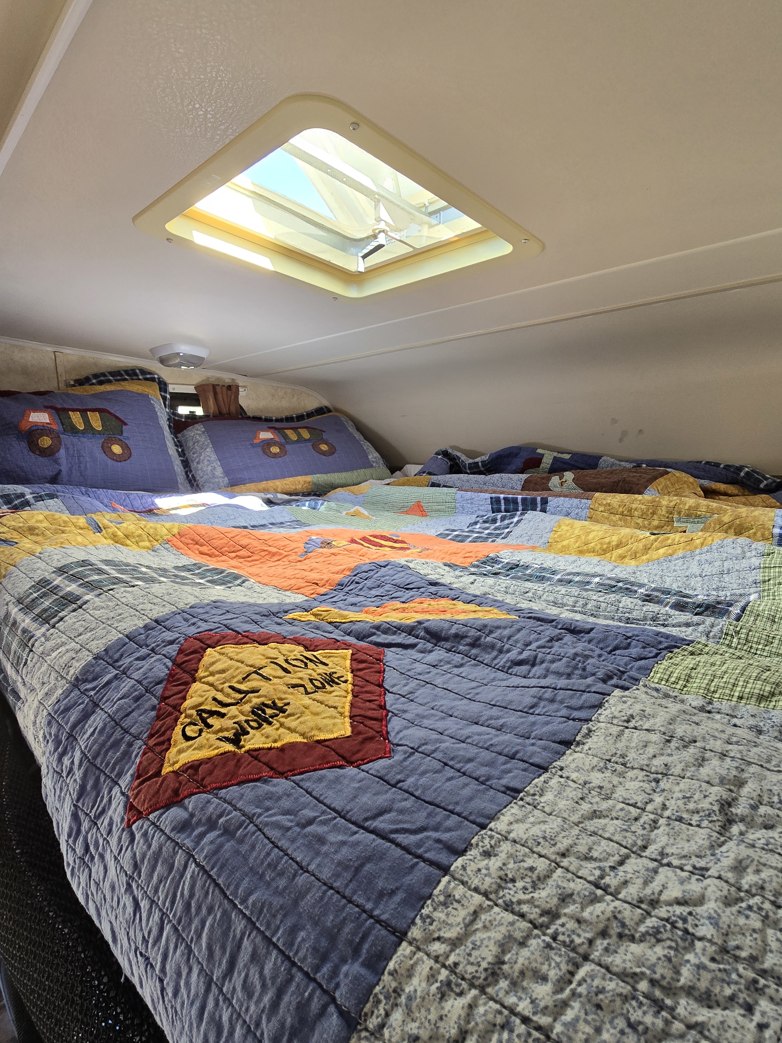 Cozy RV rental bedroom with a colorful quilt, truck-themed pillows, and a skylight providing natural light.. Forester Grand Touring 2015