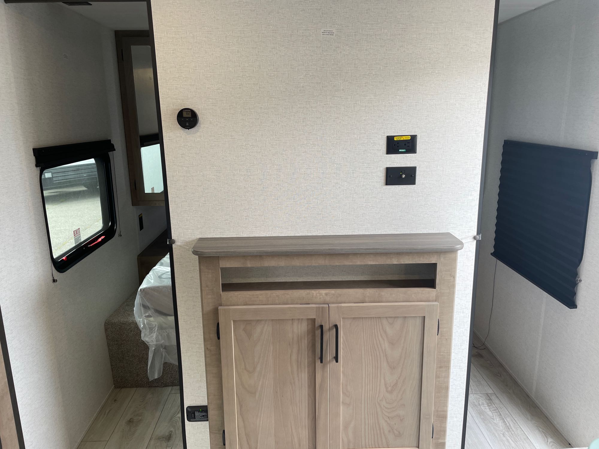 This rv rental interior features a cozy living area with an entertainment cabinet, power outlets, thermostat, & bedroom access.. Keystone Springdale Classic 261BHC 2025
