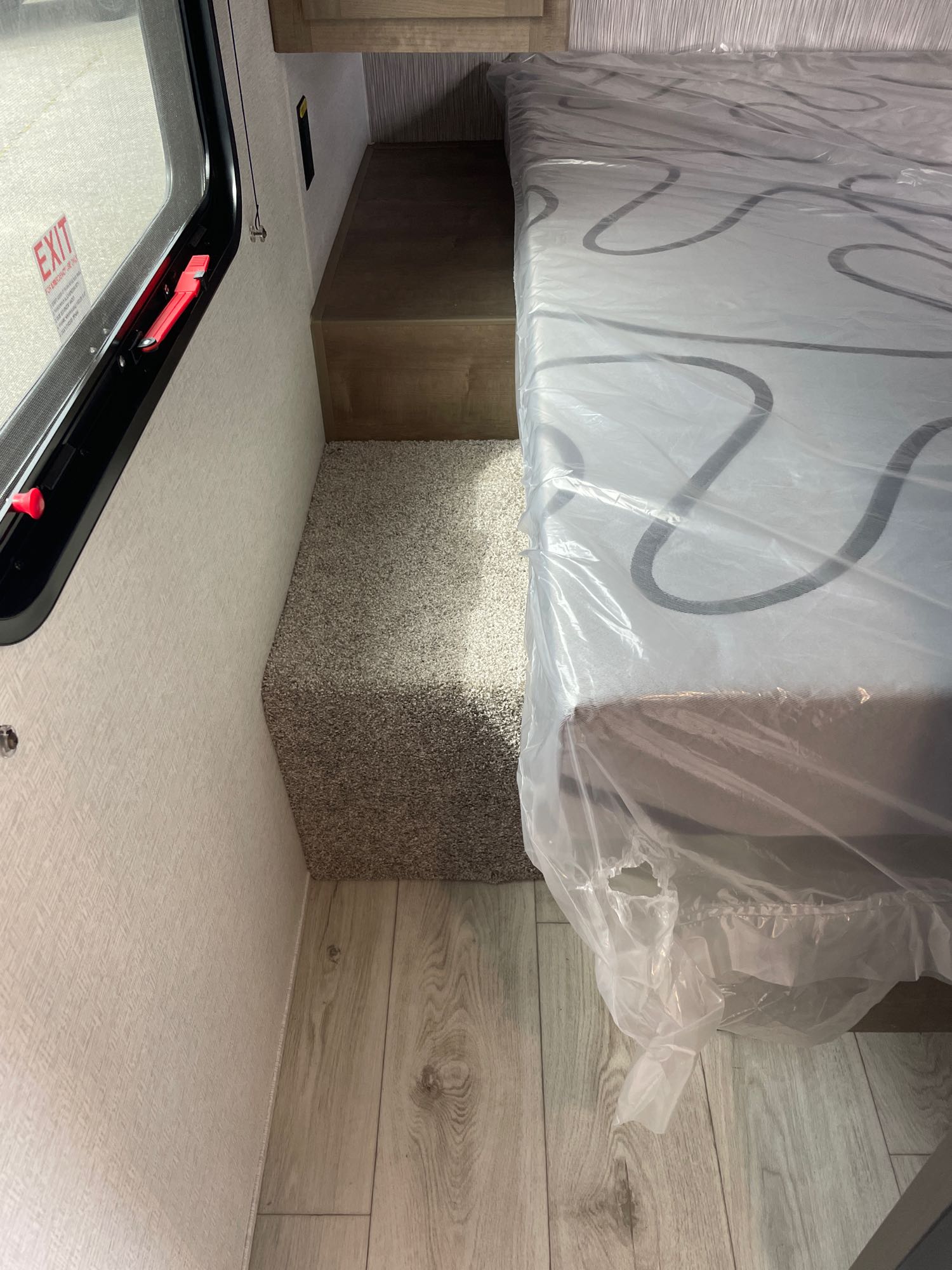 Inside an RV rental: a compact bed with a mattress in plastic, emergency exit window, and wooden flooring.. Keystone Springdale Classic 261BHC 2025