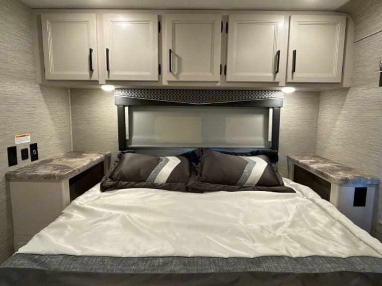 This RV rental features a comfortable bedroom with overhead storage, bedside tables, and a large bed, perfect for your next trip.. Thor Four Winds 2022