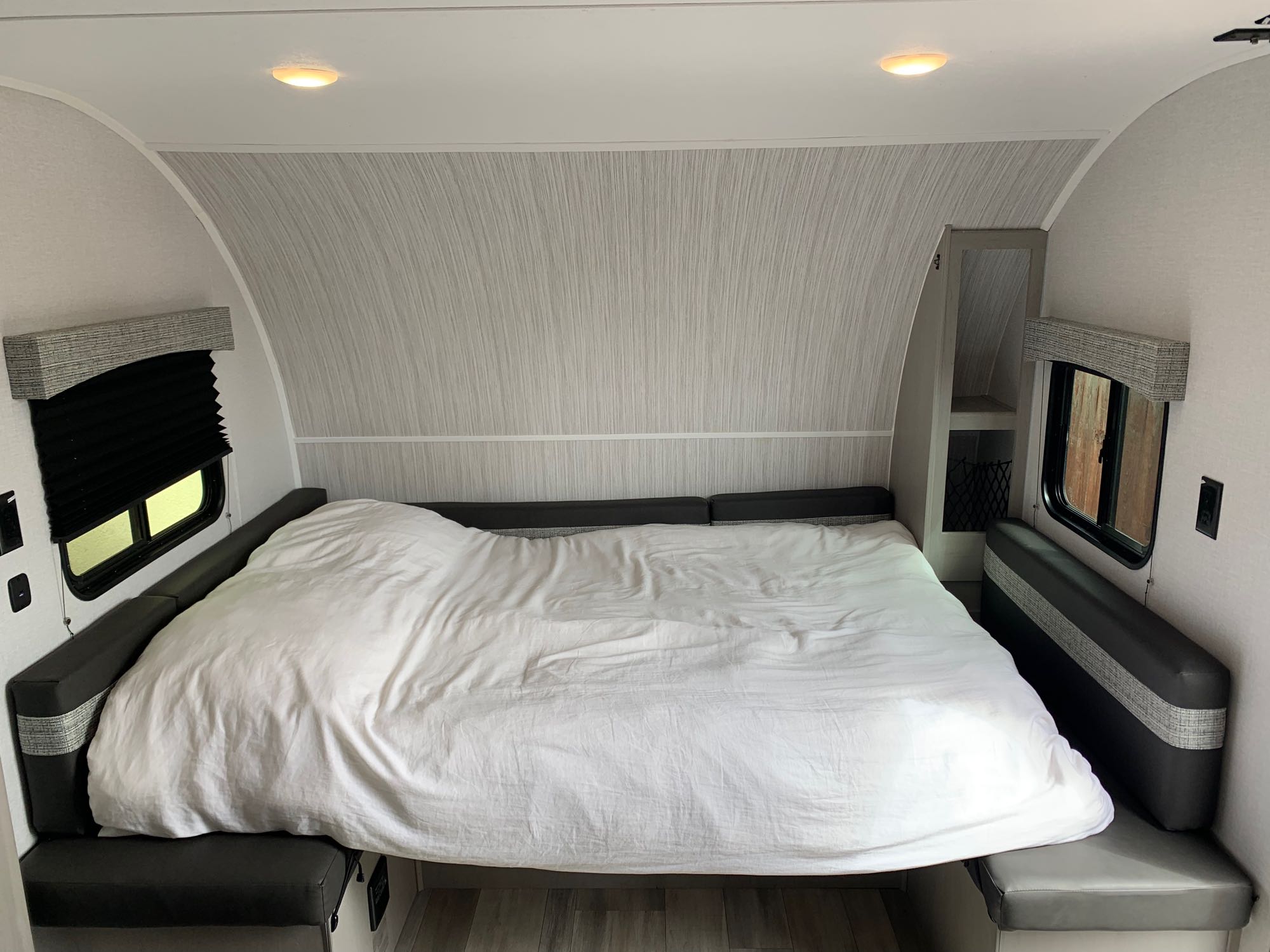 RV rental interior showcasing a comfortable bed with white bedding and integrated gray seating areas on both sides.. Clipper 18BHS 2023